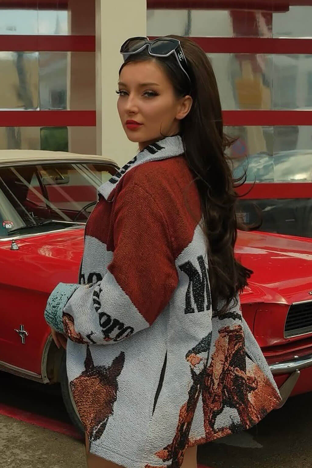 Woman with long brown hair in a patterned coat standing in front of a red car. Brown half wig hairpiece, full, long with gentle waves: Taya chestnut brown 8