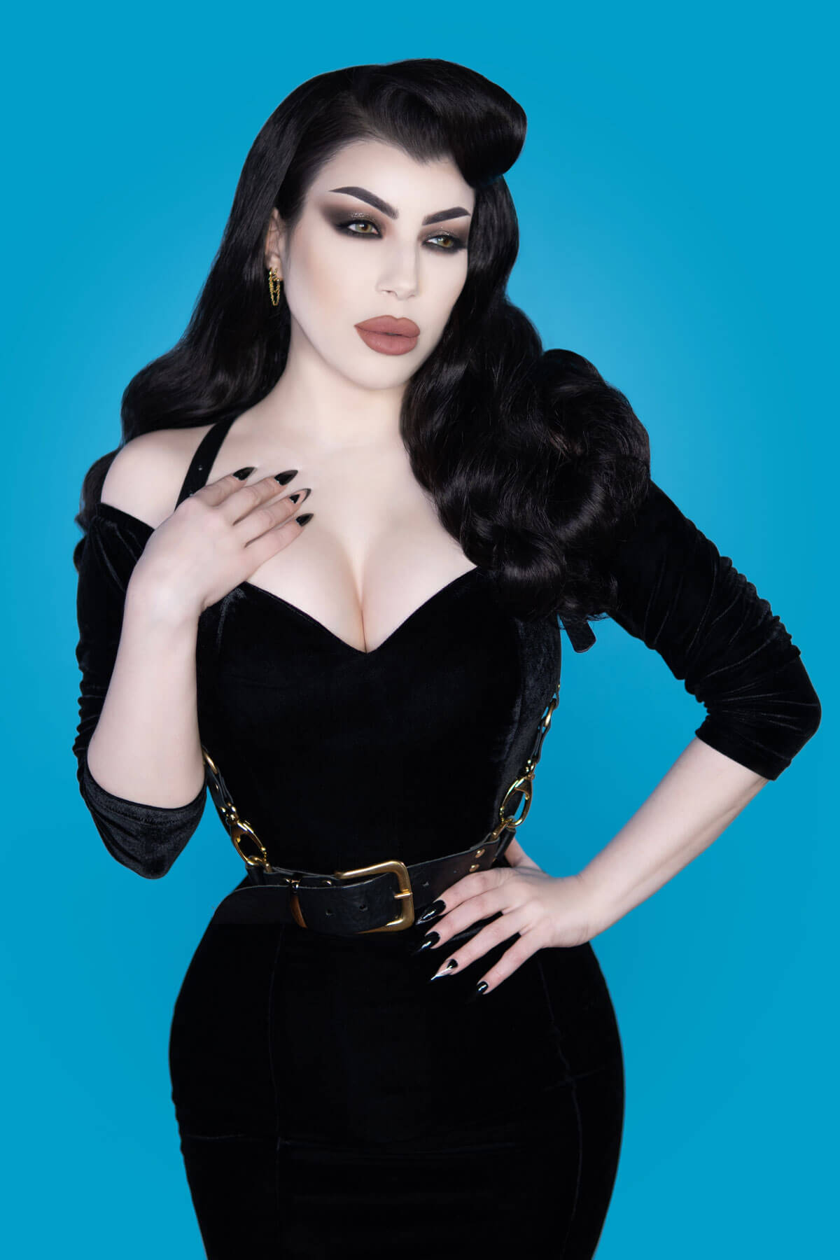 Woman in a black outfit with a gold belt against a blue background. 1950s style half wig hairpiece with beautiful waves: Morgana auburn BO