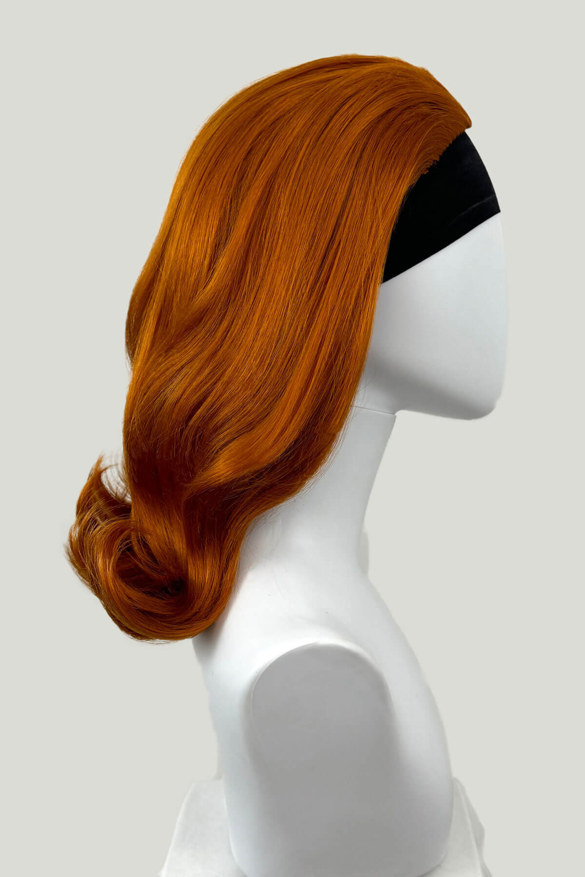 Orange wig on a mannequin head against a white background. 1960s half wig hairpiece, flicked, hair flip: Philippa ginger
