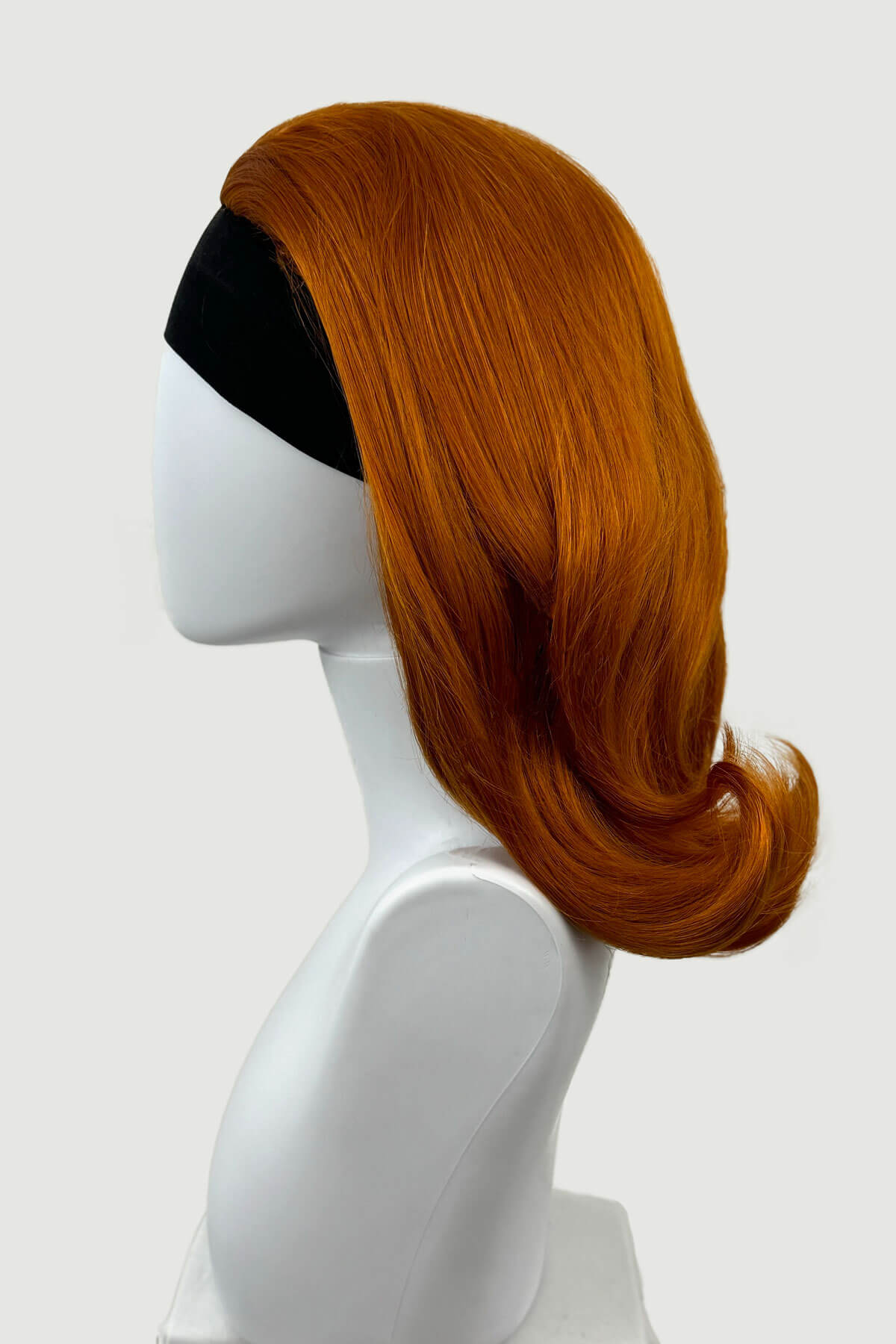 Reddish-brown wig on a mannequin head against a white background. 1960s half wig hairpiece, flicked, hair flip: Philippa ginger