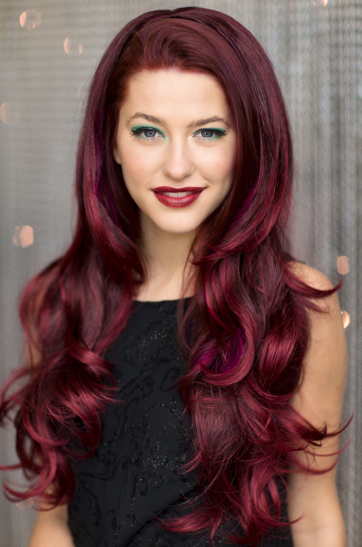 Woman with long, wavy, burgundy hair against a neutral background. Black and red half wig hairpiece (3/4 wig), loose curls: Monica