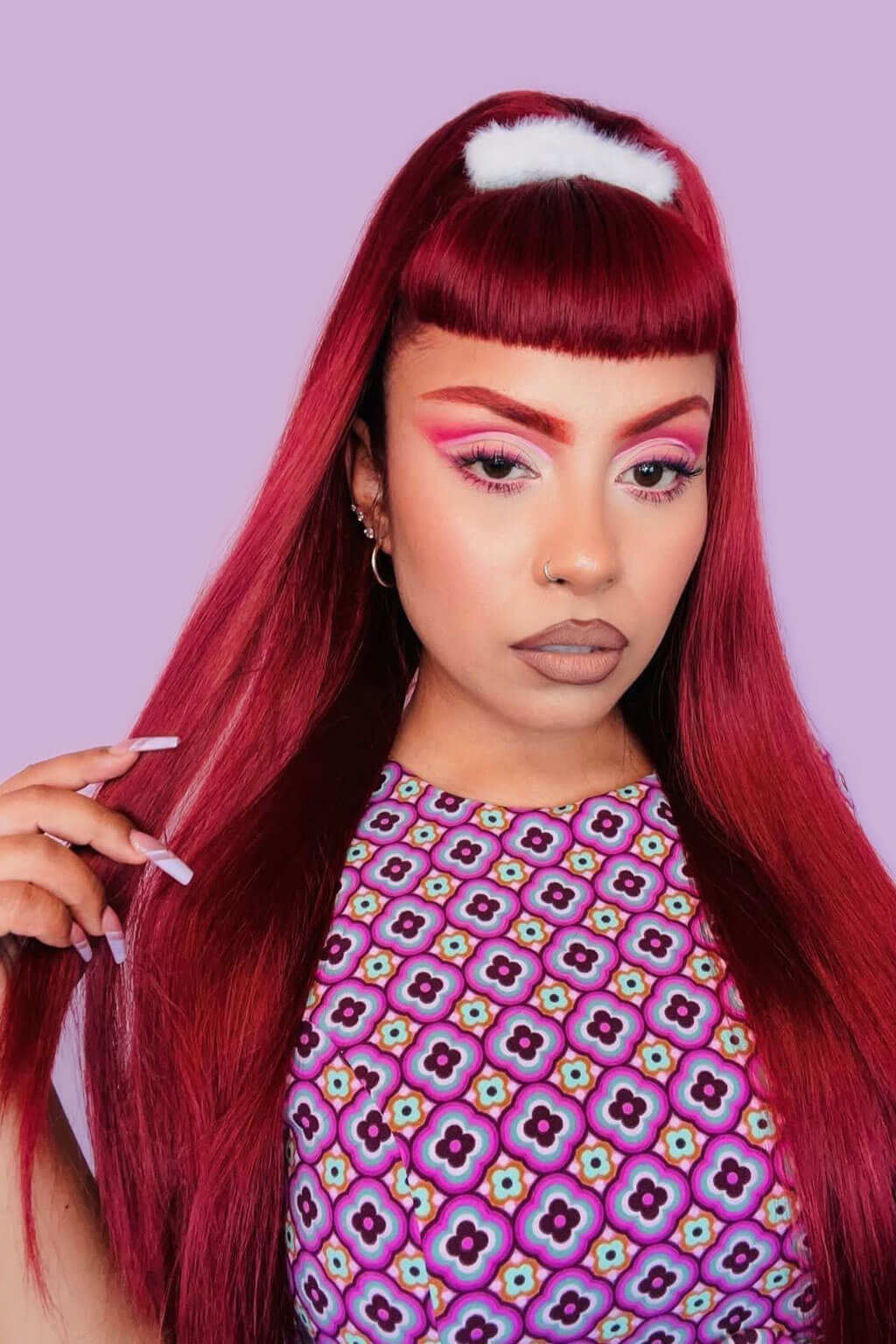 Woman with vibrant red hair and colorful makeup against a light purple background. 1960s style hair, high crown long straight half wig: Andrea cherry red 39