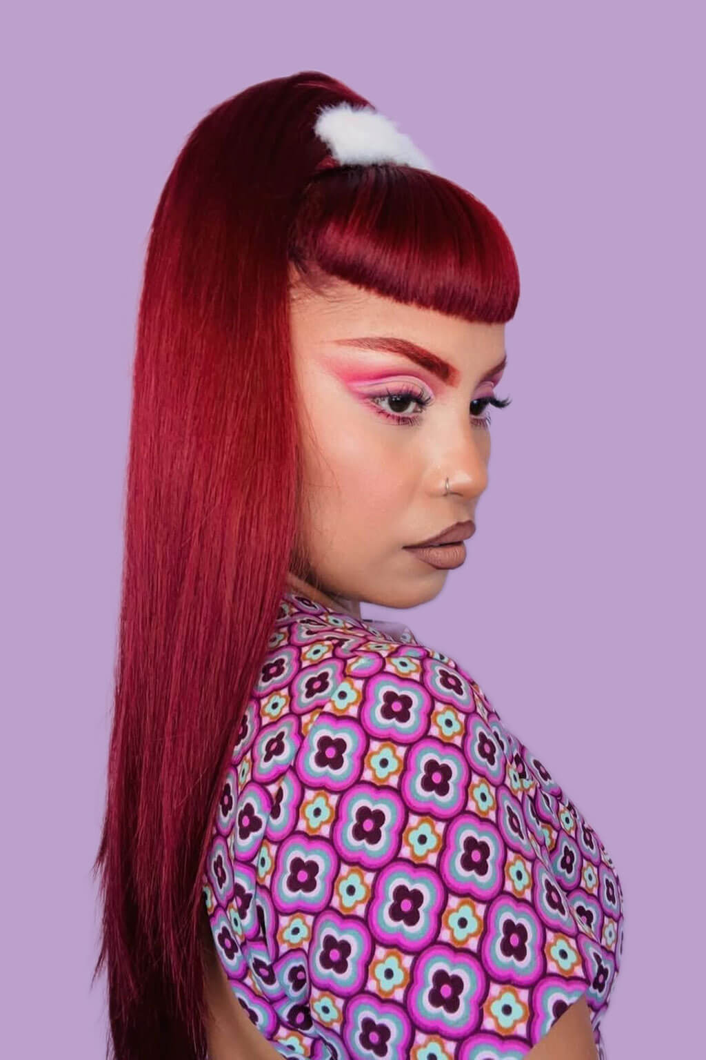Person with red hair and colorful patterned shirt against a purple background. 1960s style hair, high crown long straight half wig cherry red: Andrea