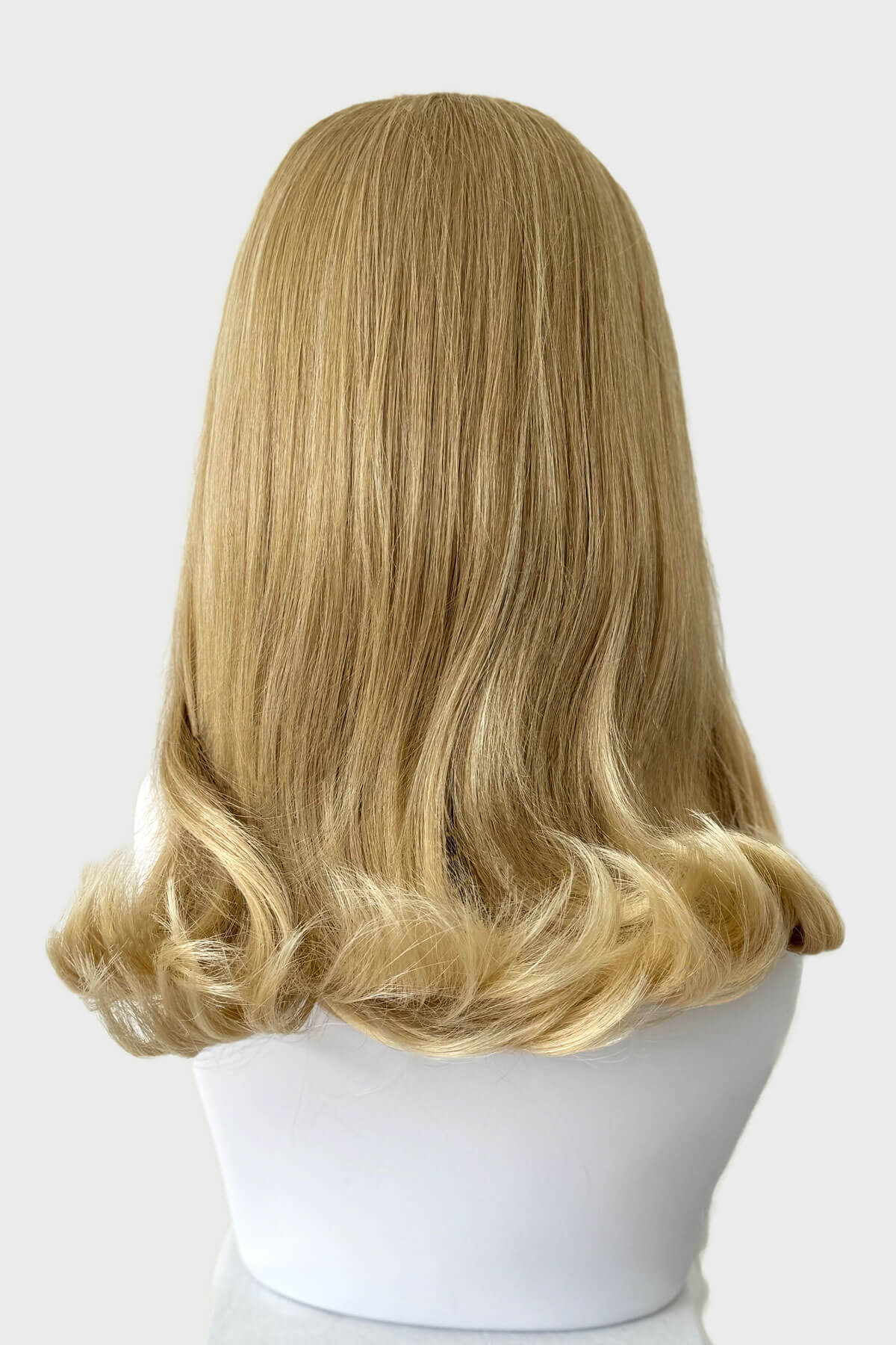 Blonde wig on a white mannequin head against a light gray background. 1960s half wig hairpiece, flicked, hair flip: Philippa blonde 613T24