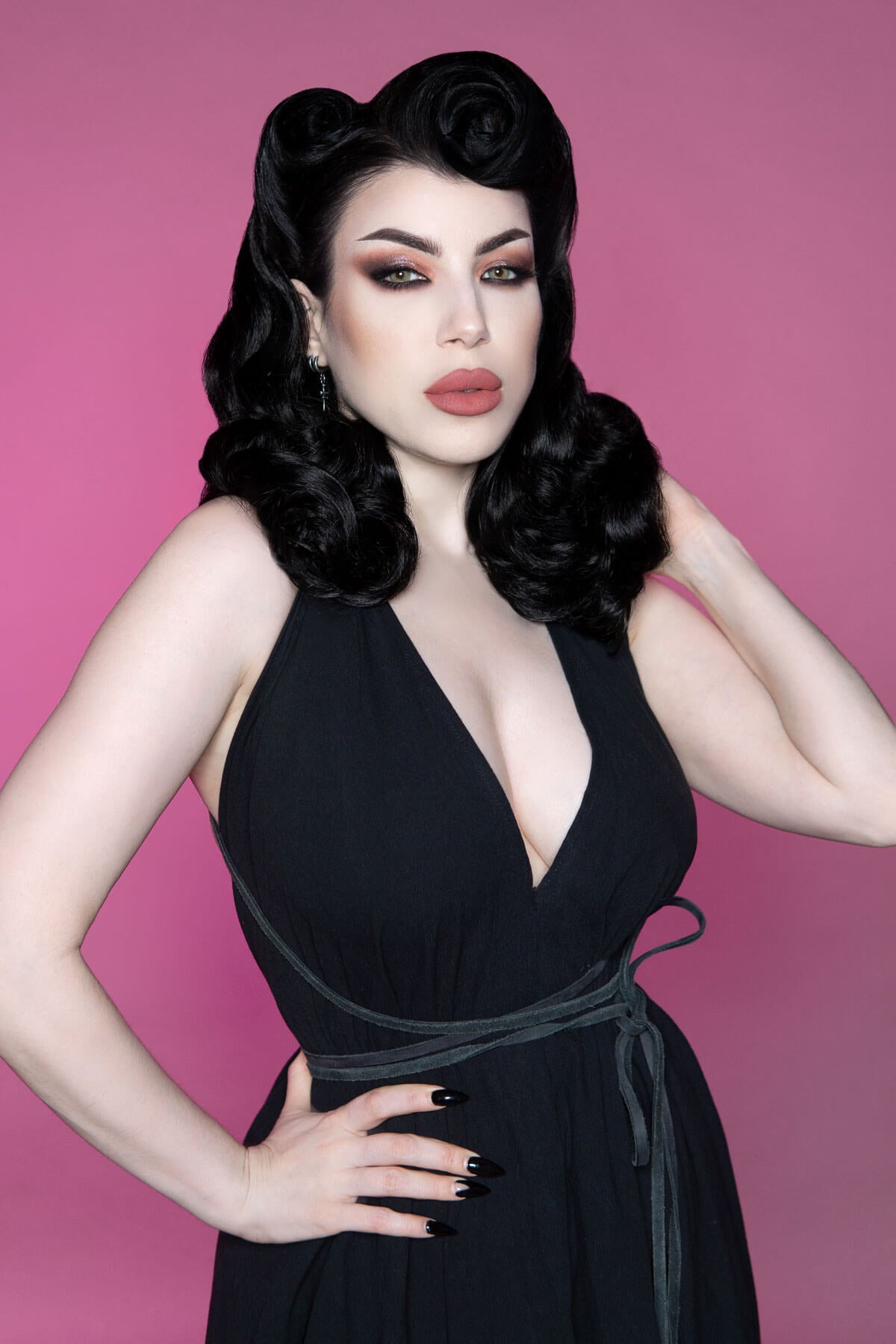 Woman in a black dress with a deep neckline against a pink background. 1950s style shoulder length half wig hairpiece with beautiful vintage waves: Onyx blond 613T24