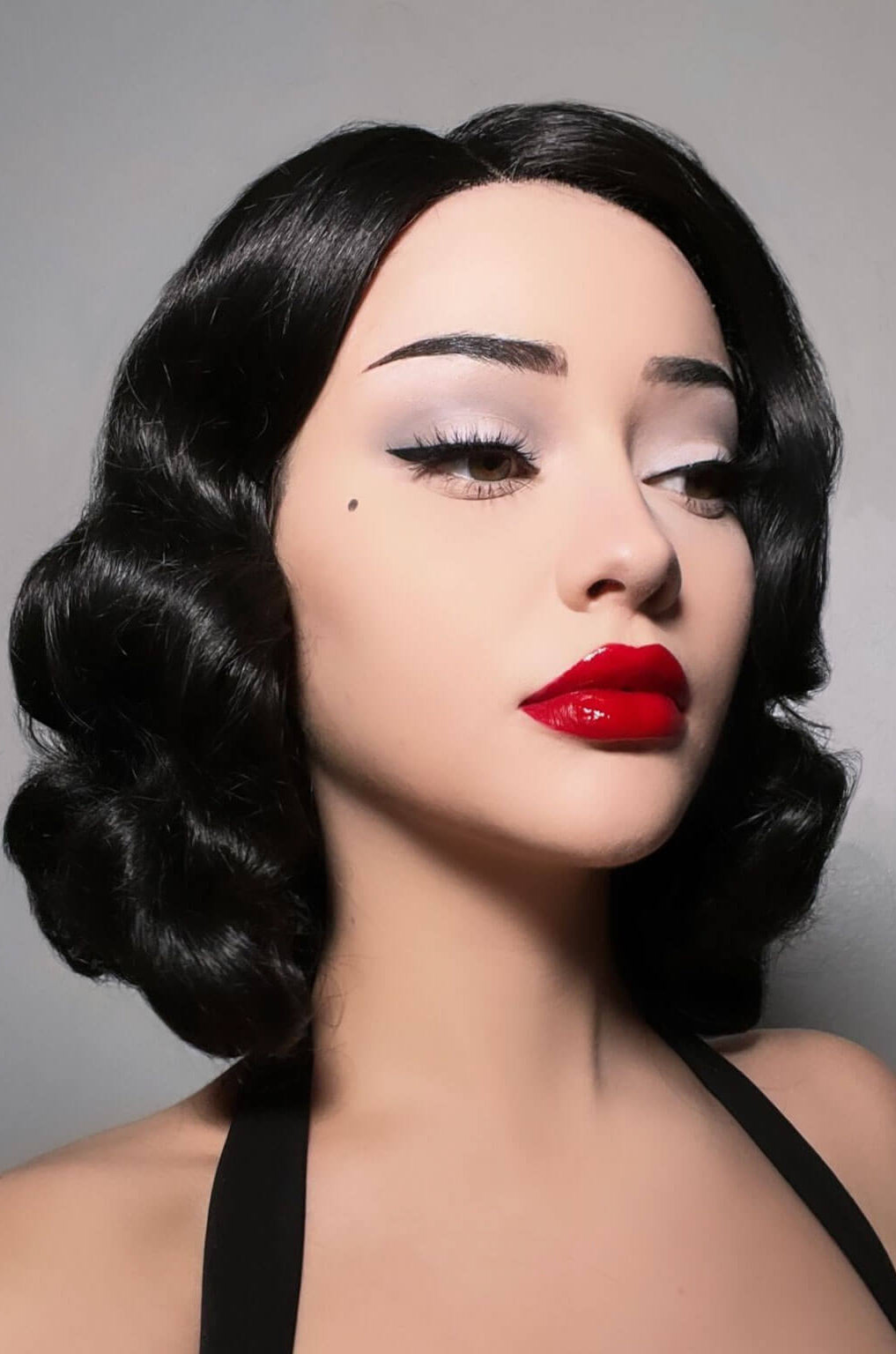 Woman with vintage-style makeup and hair against a grey background. Black lacefront wig, pinup/vintage style, mid length with finger waves: Etta