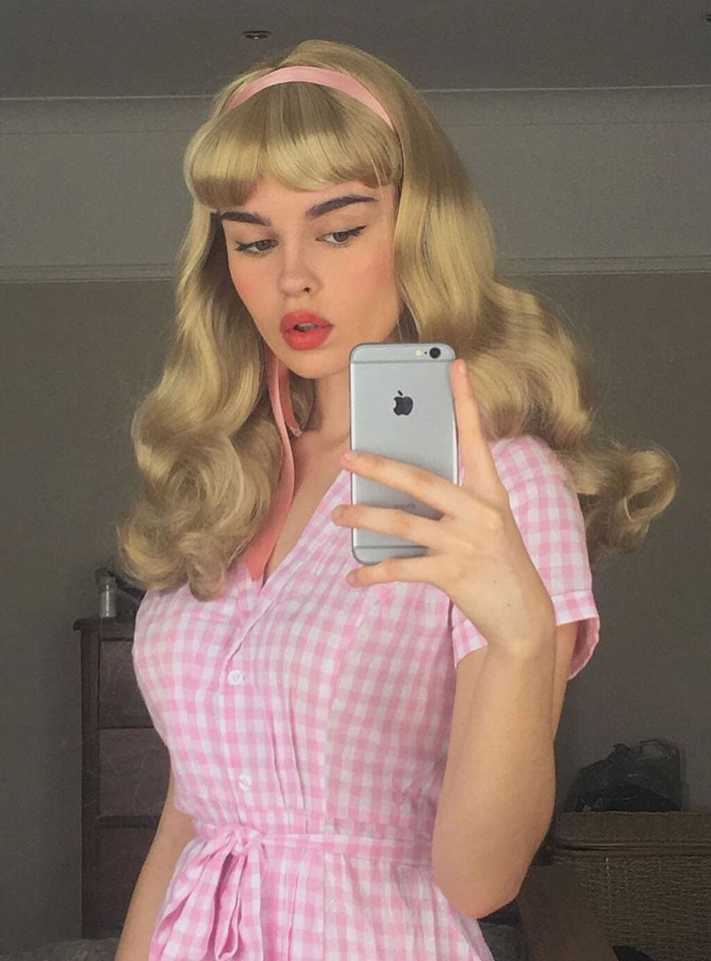Woman in a pink checkered dress taking a mirror selfie. Long blonde 1950's style wig, gently wavy with short fringe: Emmeline