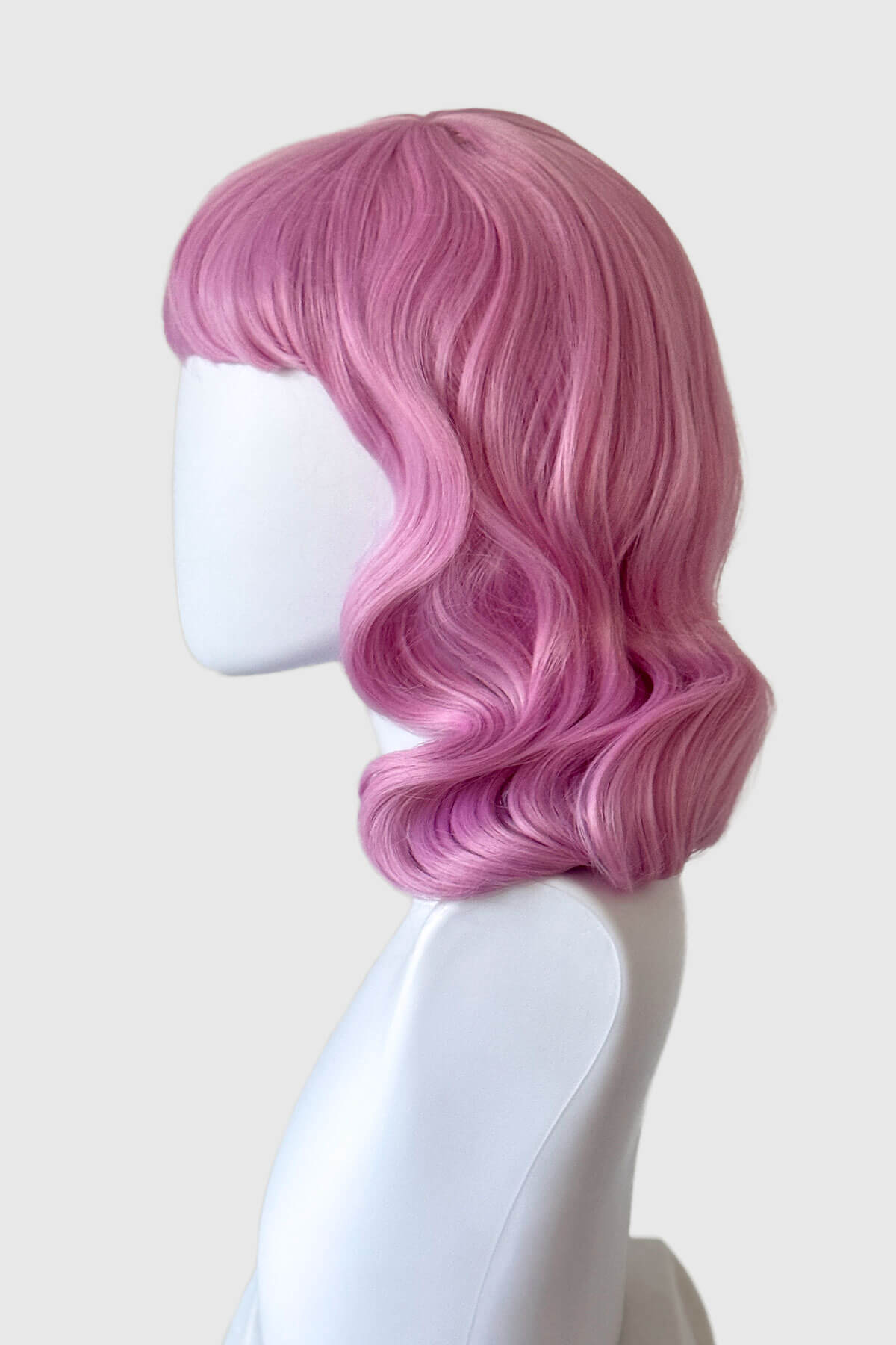Pink wig on a mannequin head against a white background. Pink pinup style wig, with finger waves and a short fringe, 1950s style: Stevie light pink 2614