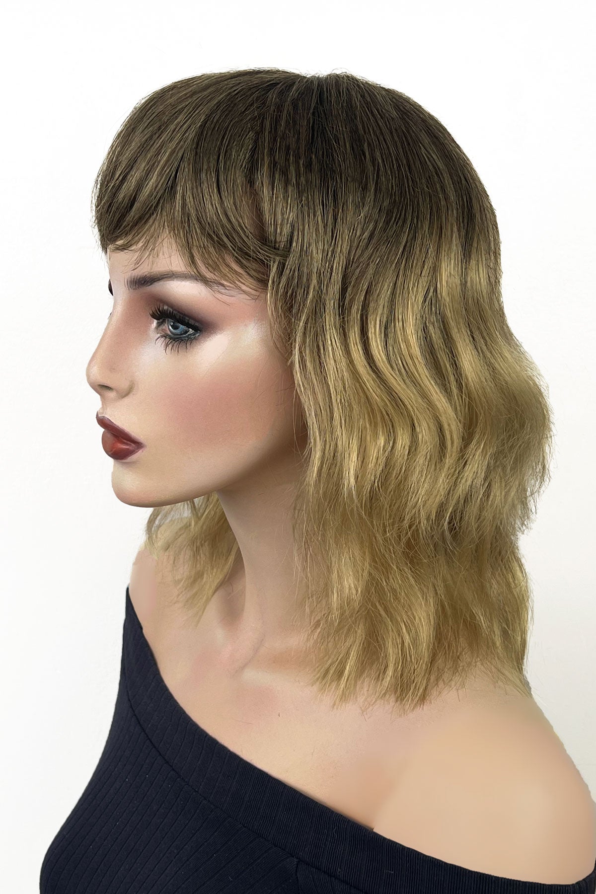 Woman with wavy hair and bangs on a white background. Long bob wig (LOB) with textured waves, blended from chestnut brown to blonde: Lili