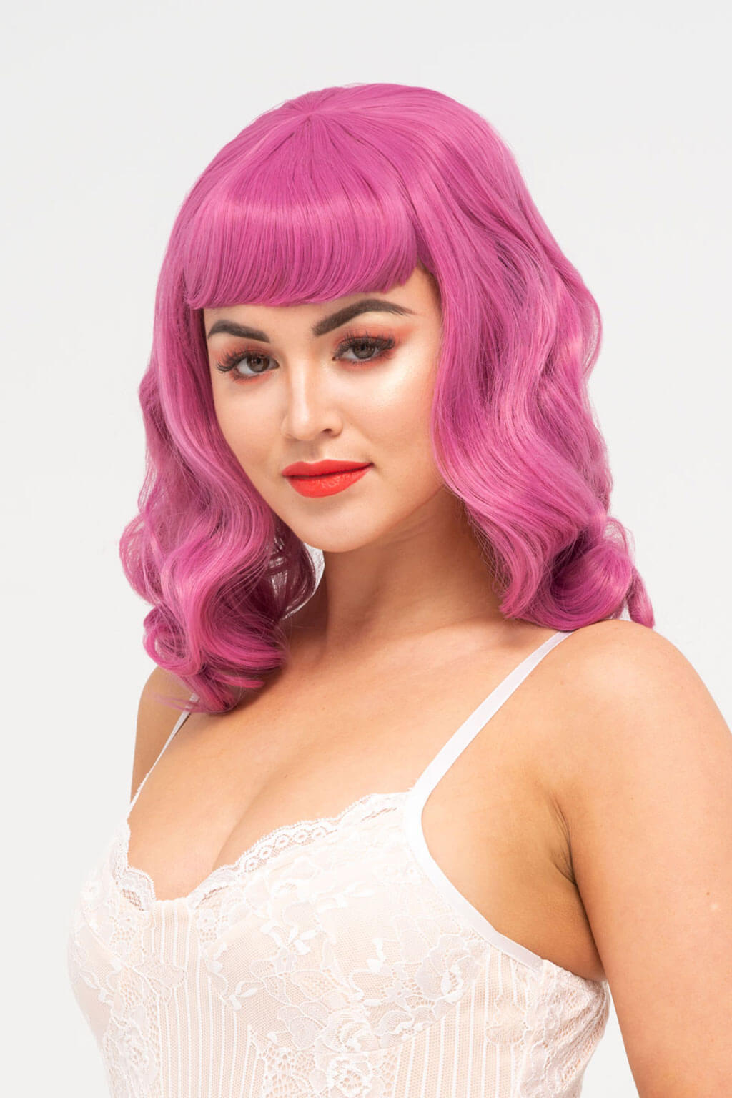 Woman with pink wig and red lipstick on a white background. Pink pinup style wig, with finger waves and a short fringe, 1950s style: Stevie dark pink 2520J