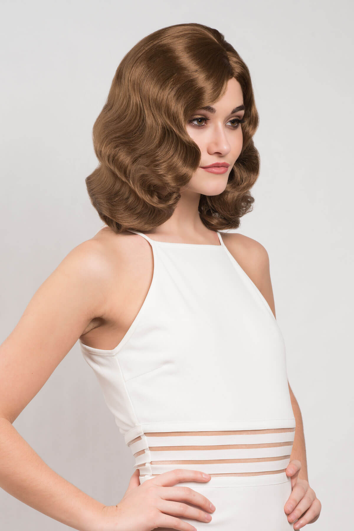 Woman with vintage-style brown hair wearing a white dress with sheer straps on a light gray background. Brown 1940s pinup style wig, with finger waves: Honey light brown 12