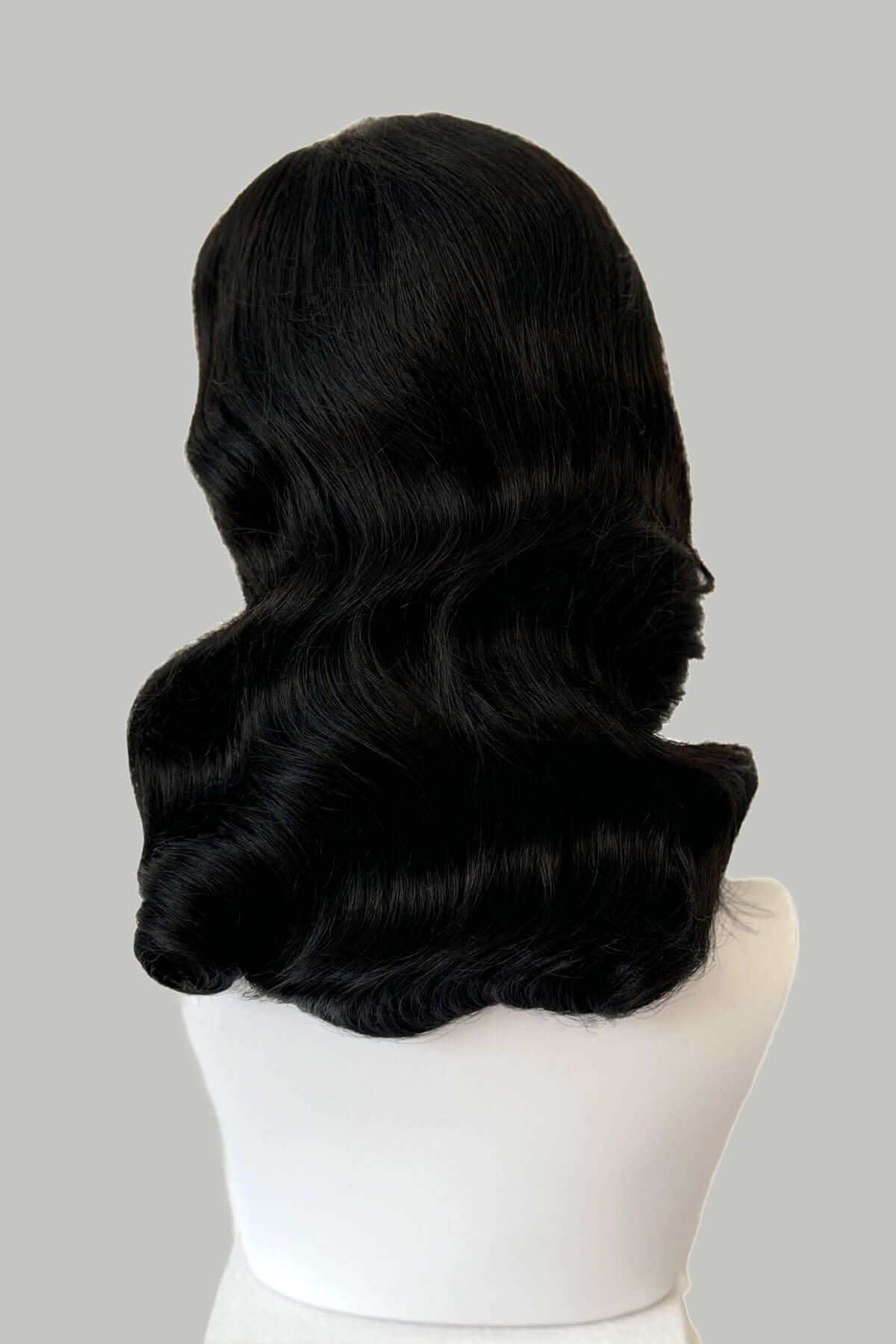 Black wig on a white mannequin head against a plain background. Black 1940s style wig with long marcel waves: Vivienne