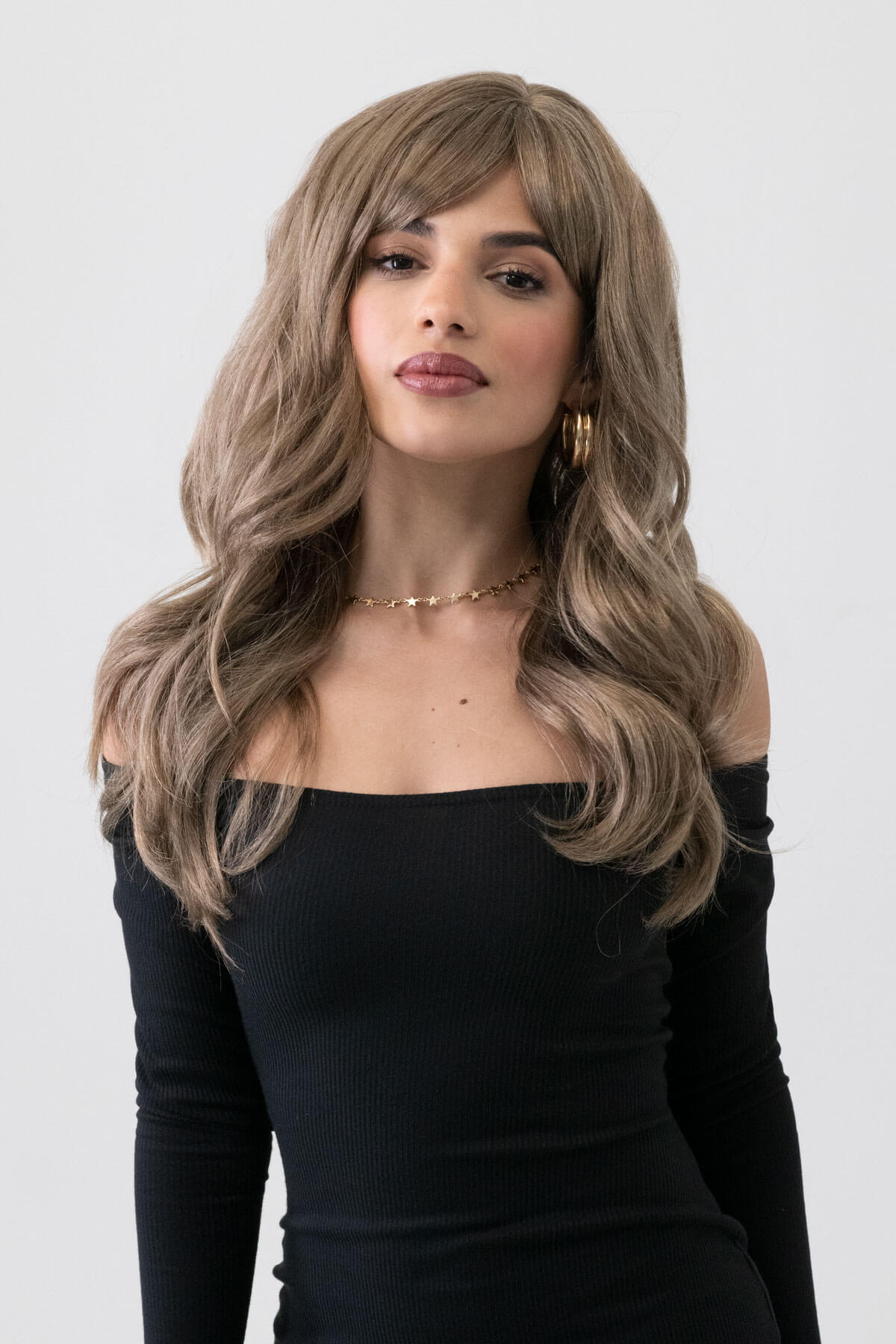 Woman wearing a wig with a neutral background. Light brown wavy wig with ash blonde highlights: Cata