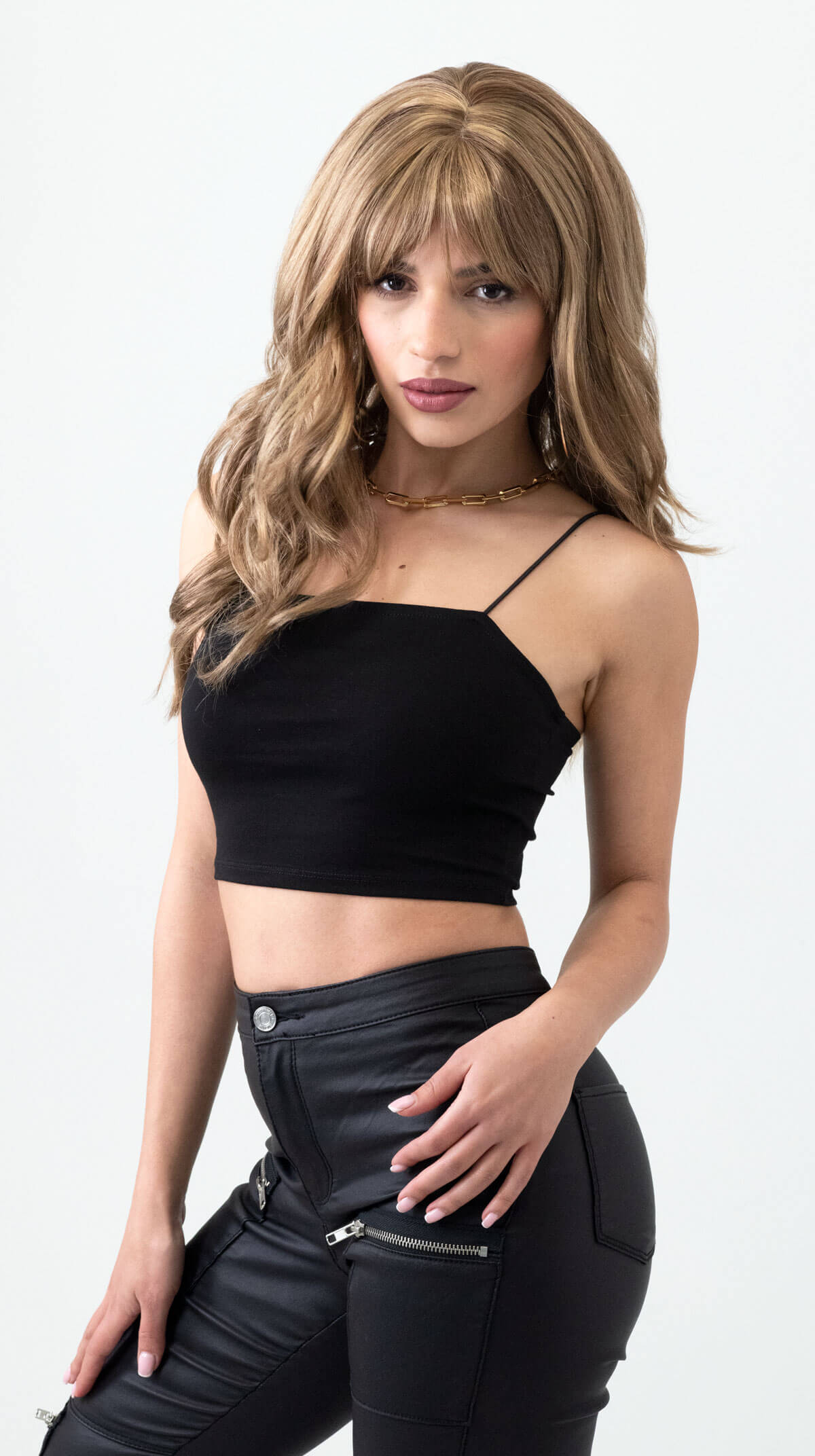 Woman wearing a black crop top and black pants on a white background. Long brown wig with blonde highlights and gentle waves: Darcy