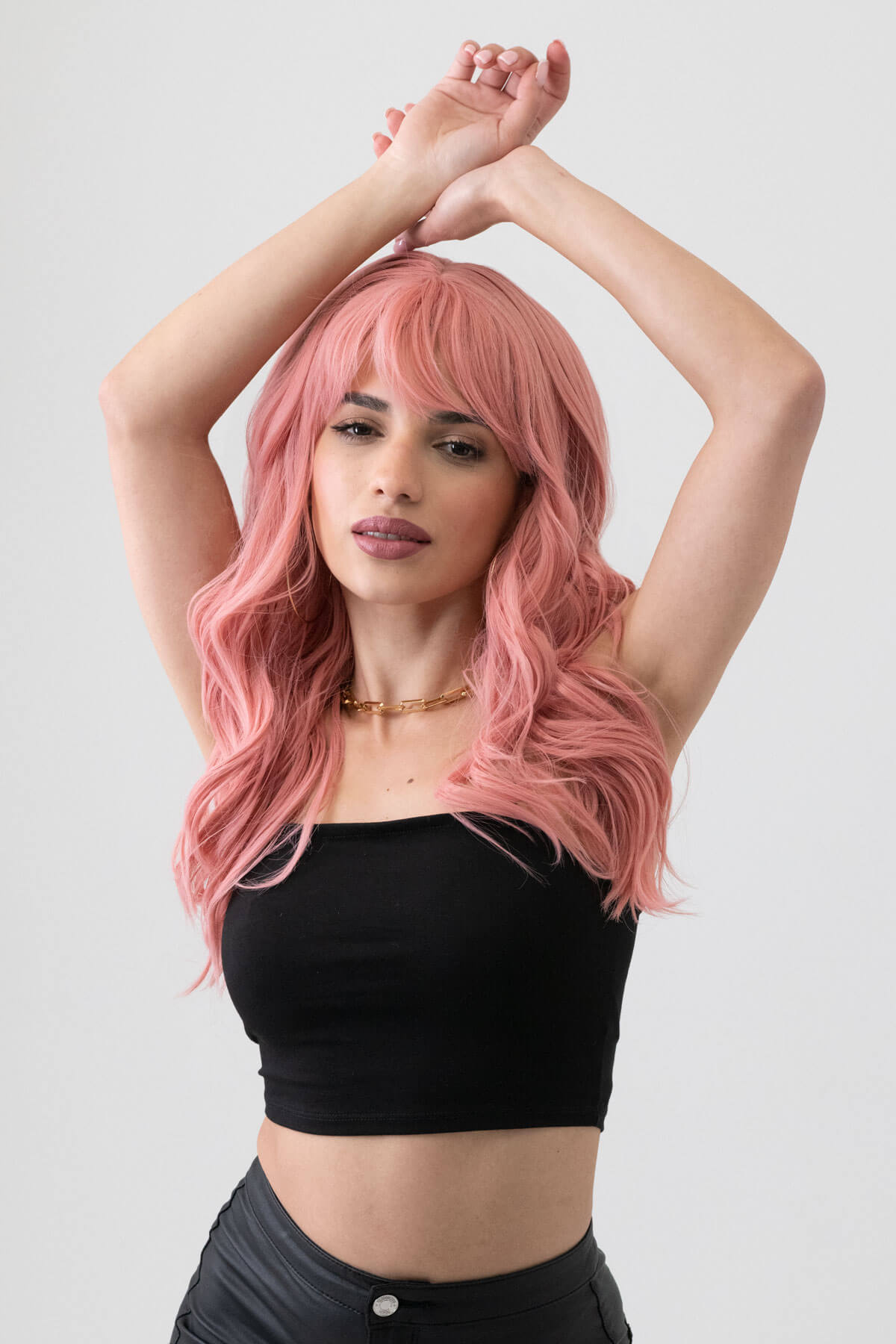 Woman with pink hair wearing a black top on a white background. Dusty pastel pink wig with long cascading waves: Rosalie