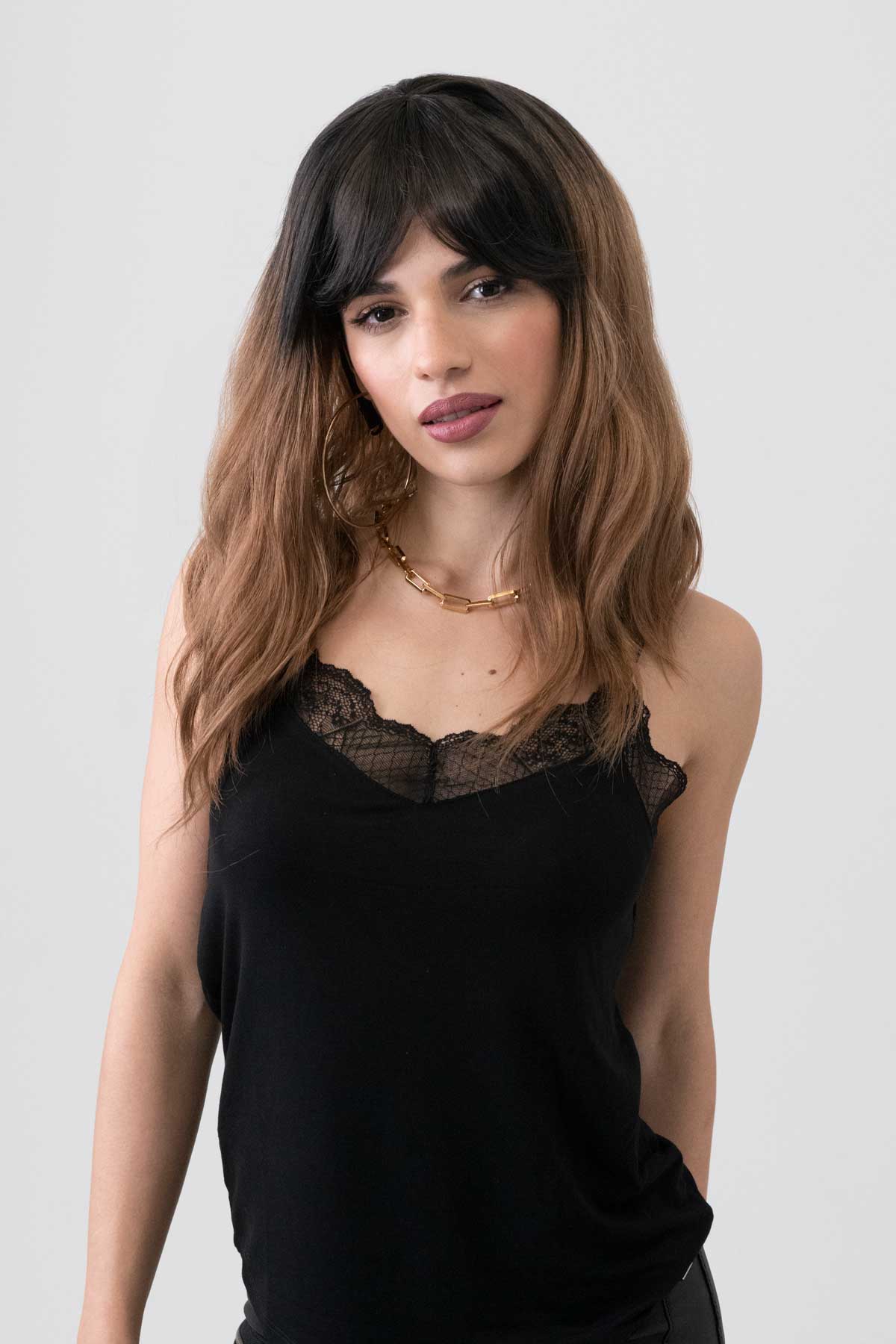 Woman wearing a black top with lace details on a white background. Long wavy bob wig (lob), dark brown to light brown ombre: Rowena