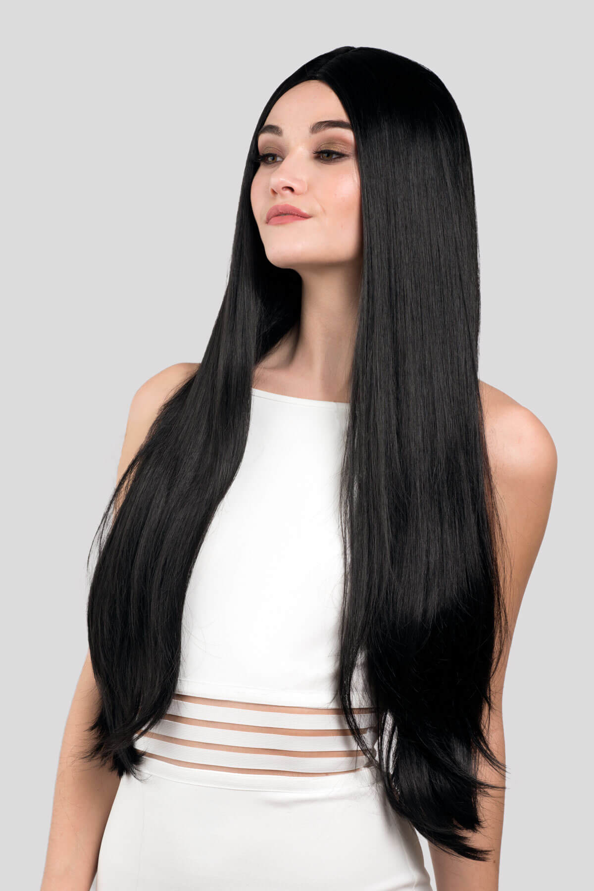 Woman wearing a long black wig on a gray background. Long straight black wig with no fringe: Madeline