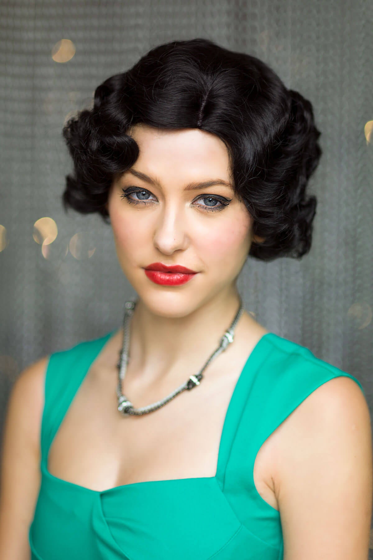 Woman with vintage-style black hair and red lipstick wearing a green dress against a gray background. Black 1920s 1930s Style Wig with Finger Waves: Cassie