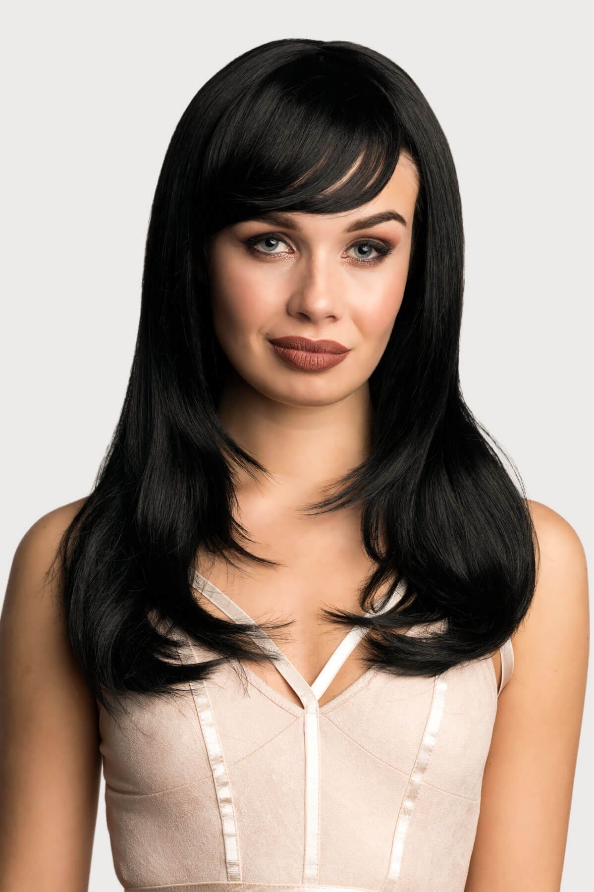 Woman with long black hair wearing a beige top on a light gray background. Long black wig, face frame style with full, sweeping fringe: Corina