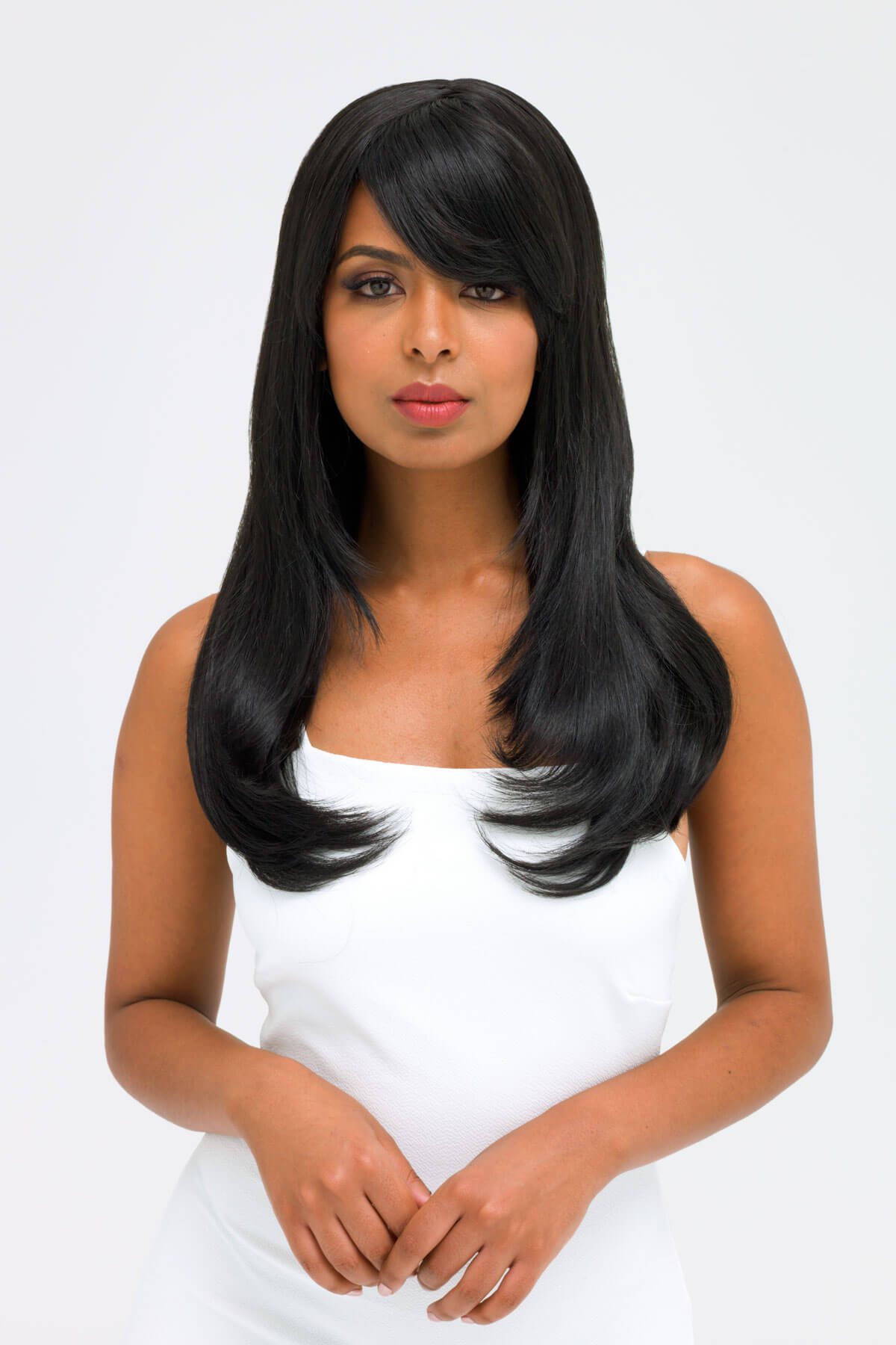 Woman with long black hair wearing a white top on a light gray background. Long black wig, face frame style with full, sweeping fringe: Corina