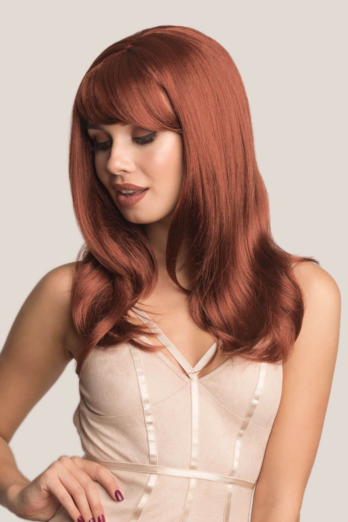 Woman with long red hair wearing a beige dress against a plain background. Long copper red wig, razor cut, face frame style: Eleanor