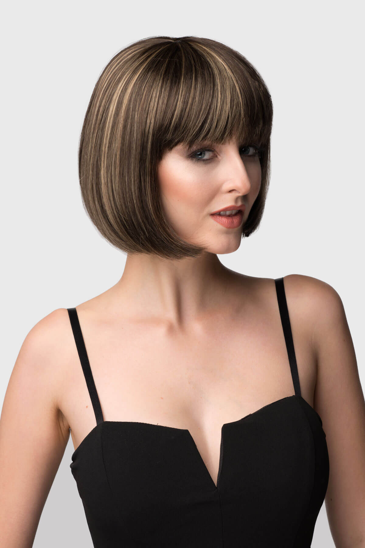 Woman with a stylish haircut wearing a black dress against a plain background. Chestnut brown bob wig with blonde highlights: Lorna