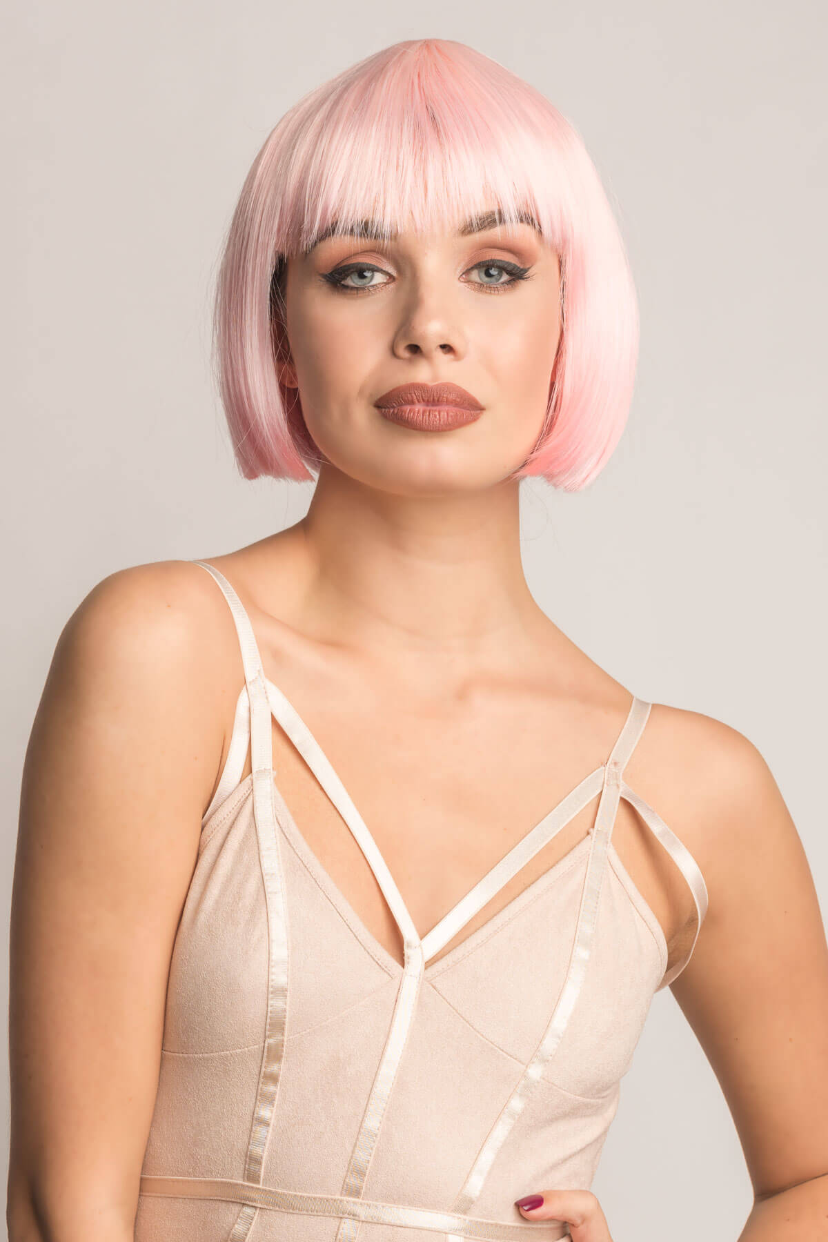 Woman with a pink bob wig wearing a sheer beige top against a light gray background. Short pink bob wig (ombre: pale pink and platinum): Louisa