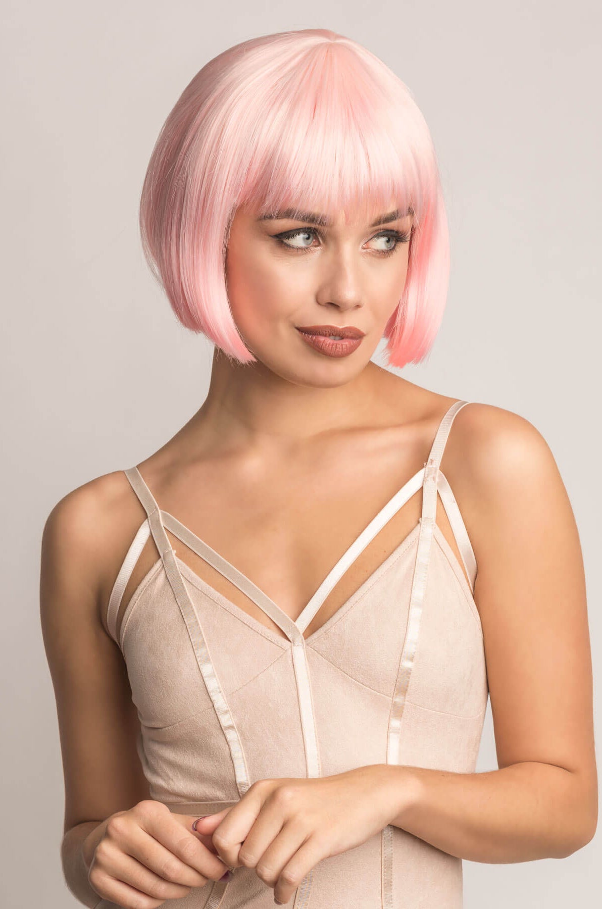 Woman with pink bob wig wearing a beige strappy top against a plain background. Short pink bob wig (ombre: pale pink and platinum): Louisa