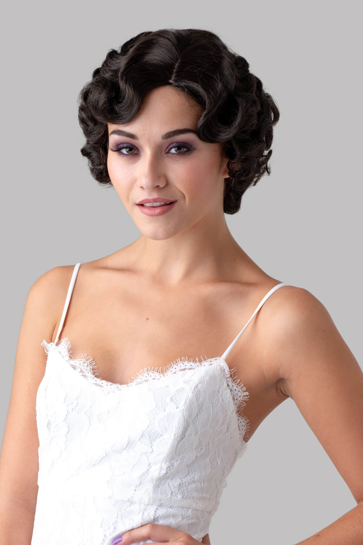 Woman wearing a white lace dress with a gray background. Brown 1920s 1930s style wig, short retro style with finger waves: Cecelia dark drown 4