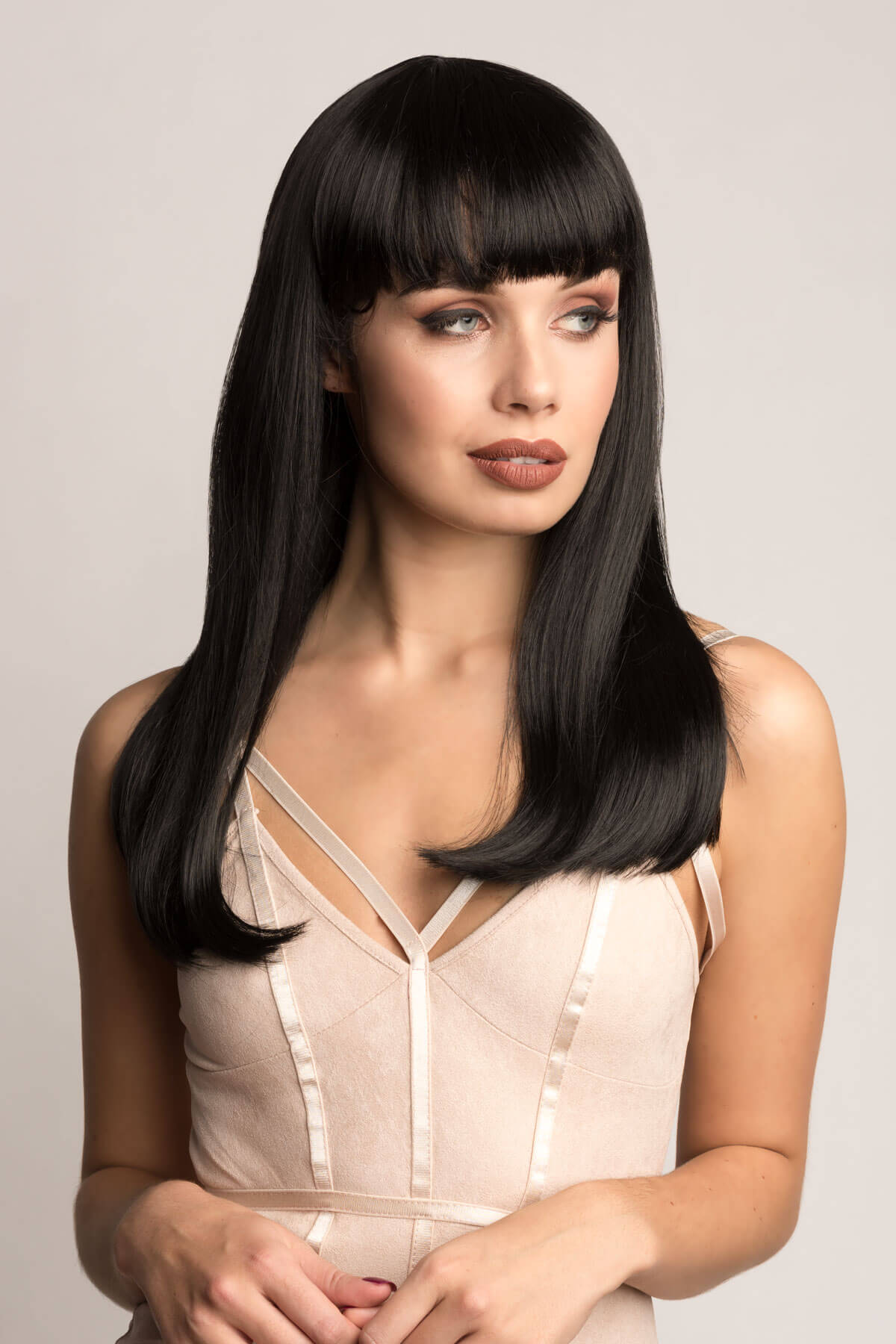 Woman with long black hair wearing a beige dress against a plain background. Long straight black wig with straight fringe: Carmen