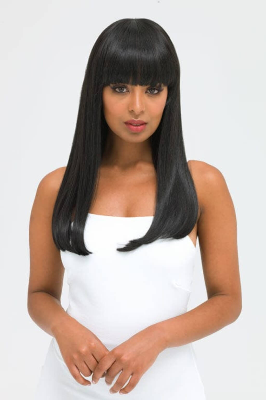 Woman with long straight black hair wearing a white top on a light grey background. Long straight black wig with straight fringe: Carmen
