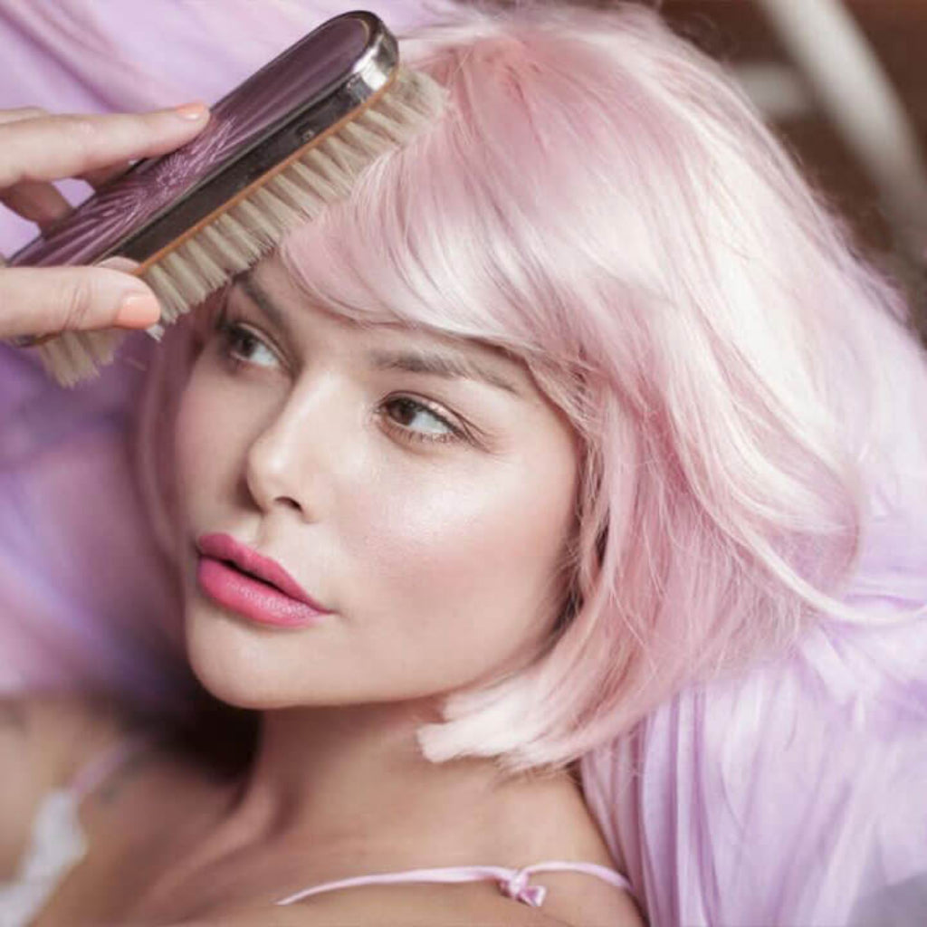 Woman with pink hair being combed by a brush, wearing a light purple top. Short pink bob wig (ombre: pale pink and platinum): Louisa