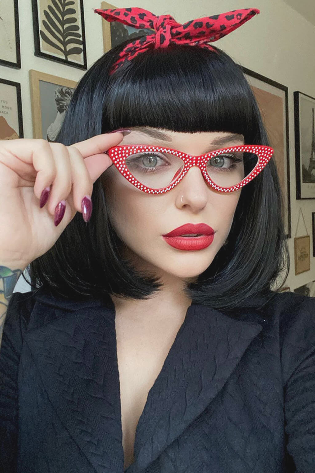 Woman wearing red polka dot glasses and a red headband. Black long bob wig with a short retro, rockabilly-style fringe: Beth