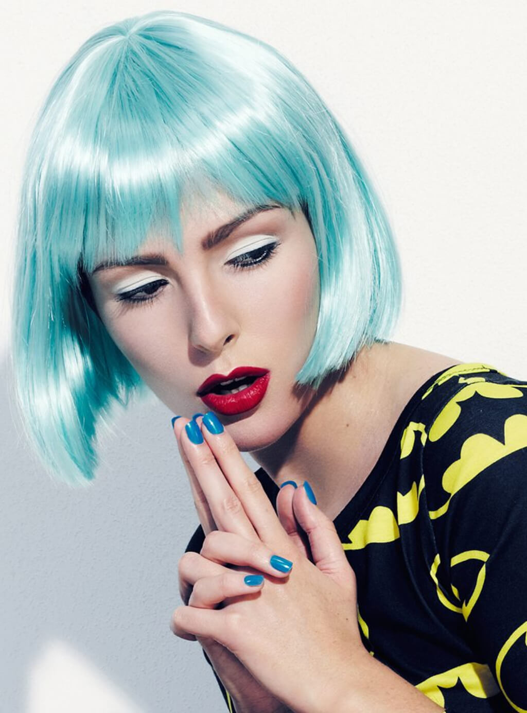 Person with turquoise hair and red lipstick posing against a light background. Turquoise bob wig with full fringe: Iris