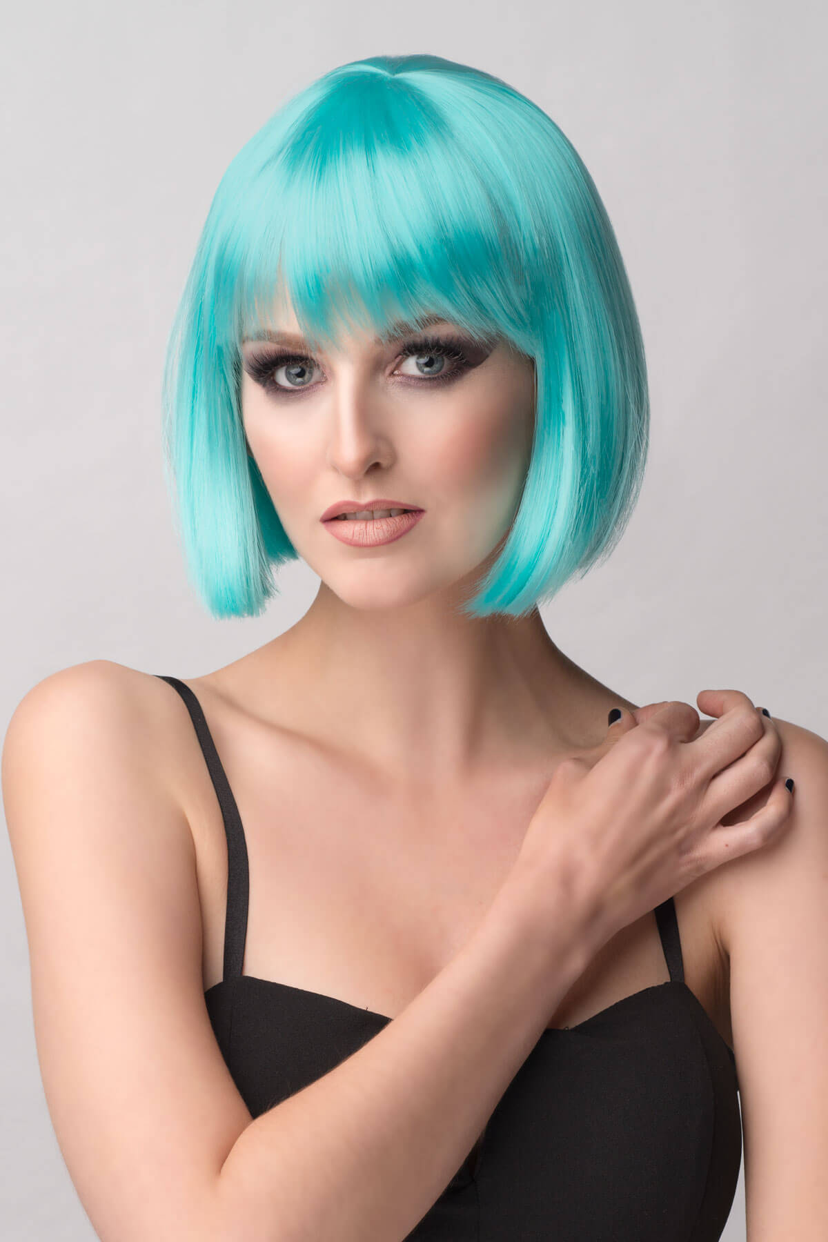 Woman with turquoise hair styled in a bob against a gray background. Turquoise bob wig with full fringe: Iris