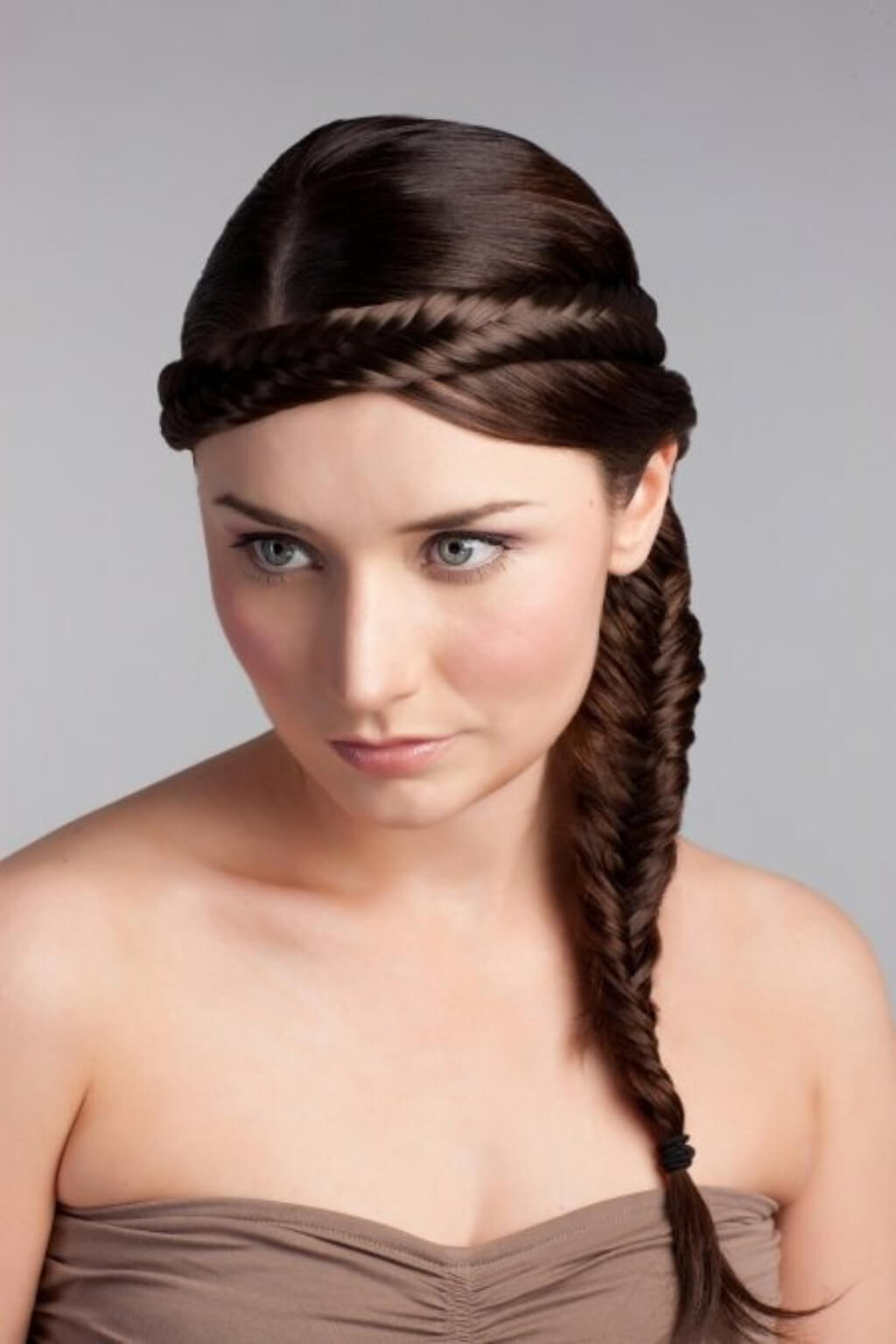 A woman wearing a fishtail plait hairband with a side braid, in a brown dress, with a neutral background. Fishtail plait hairband (braid)