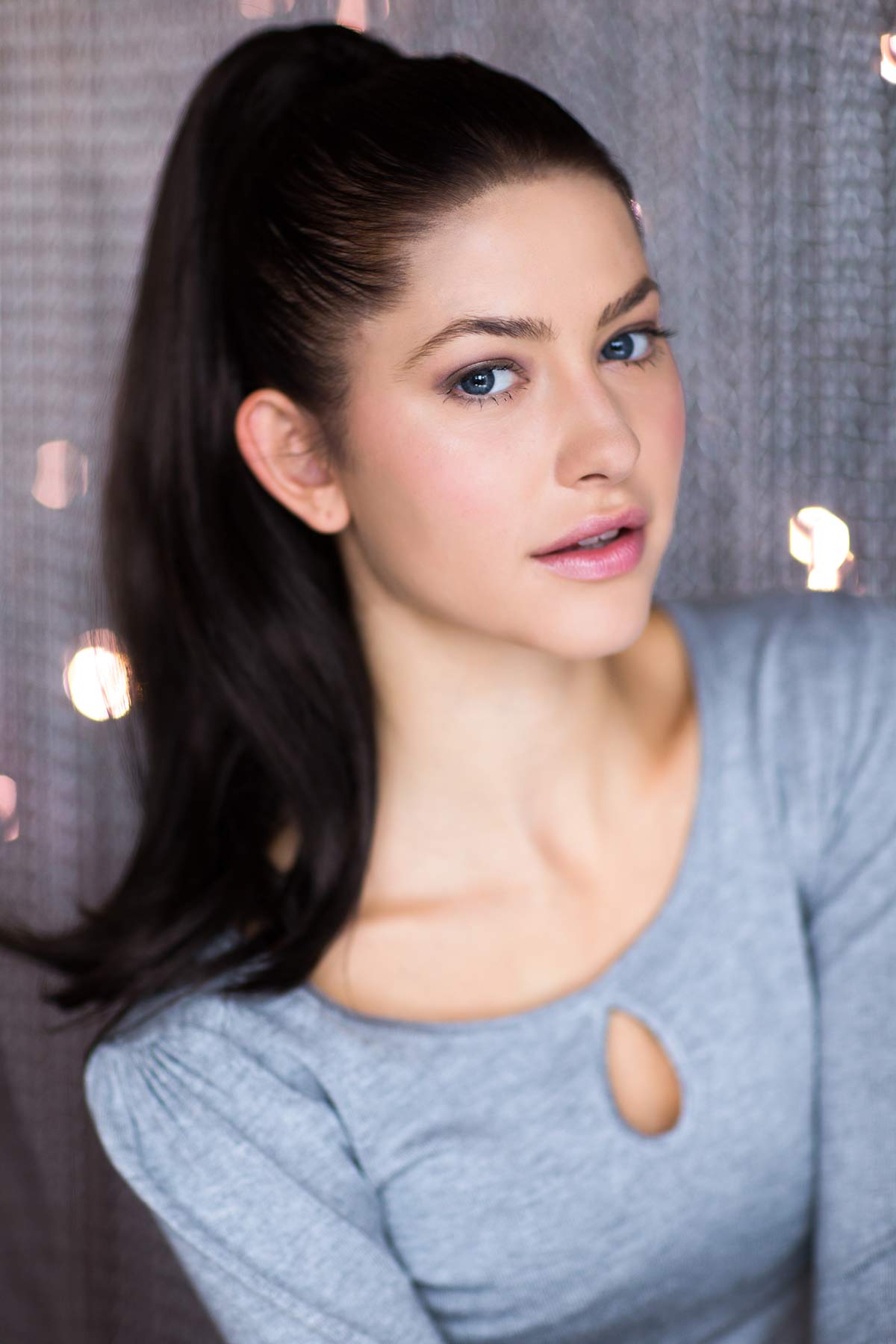 Woman with a ponytail wearing a gray sweater against a neutral background.Clip-in ponytail hairpiece extension, dark brown: Elise