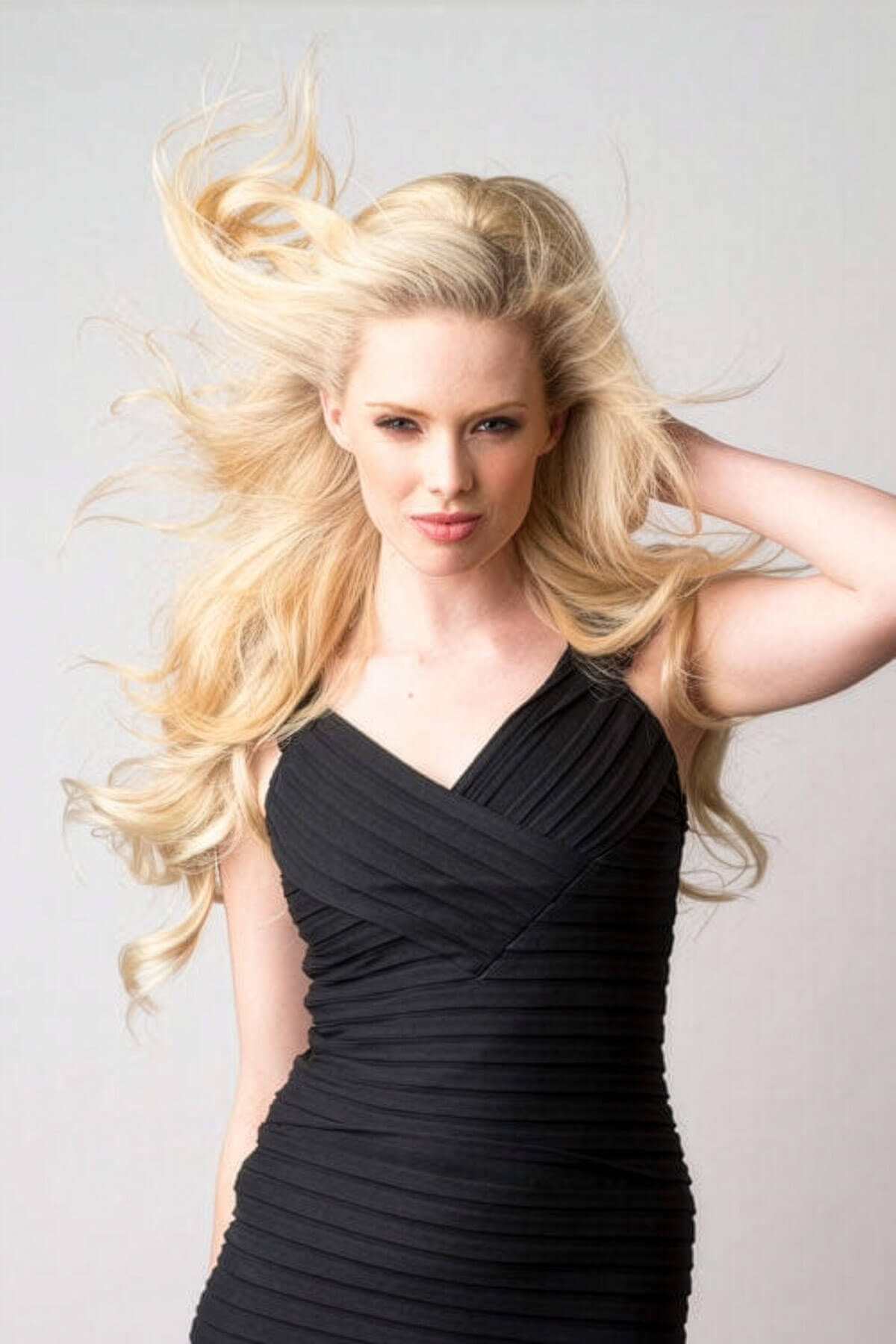 Woman in a black dress with flowing blonde hair against a light gray background. Lucky dip half wig