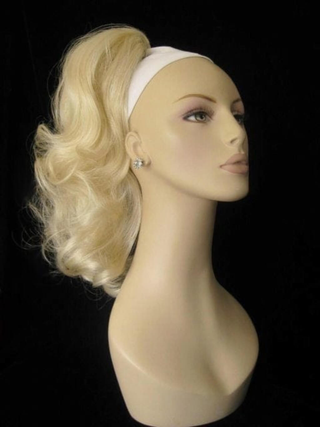 Blonde wig on a mannequin head against a black background. Curly ponytail extension clip-on hairpiece: Tulisa blonde 613