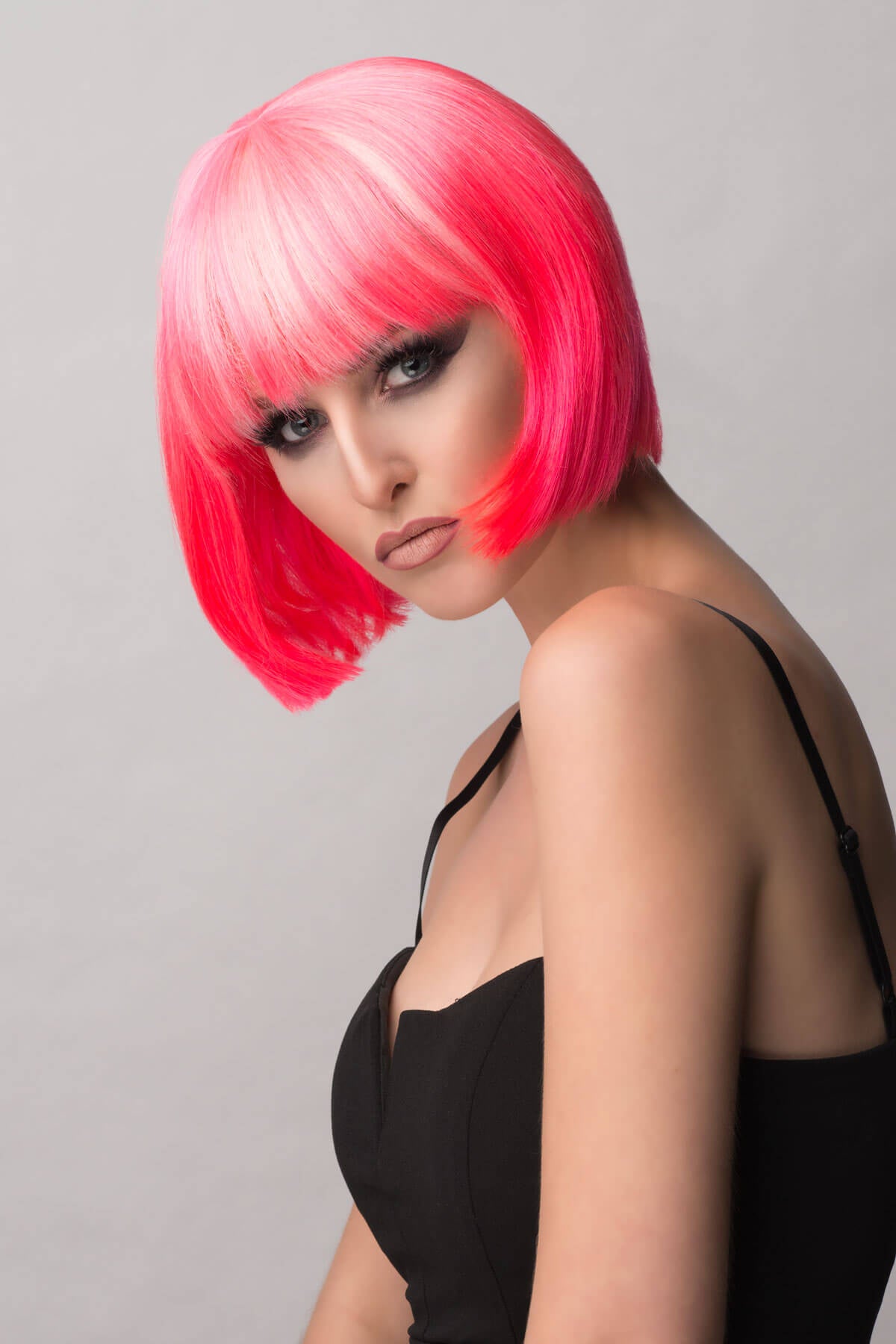Woman with bright pink hair wearing a black top against a gray background. Hot pink / light pink ombre pink bob wig, short and chic: Alma