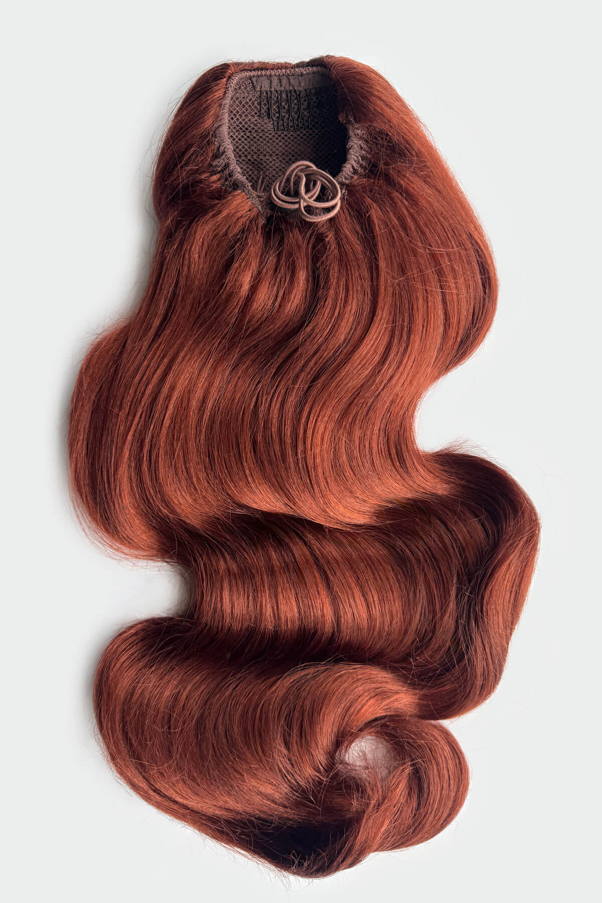 A wavy, body-wave style hair extension piece with a mesh base and a draw string attachment, shown against a light grey background. Copper red hair extension on a white background. Double volume hairpiece extension: Naomi copper red 130