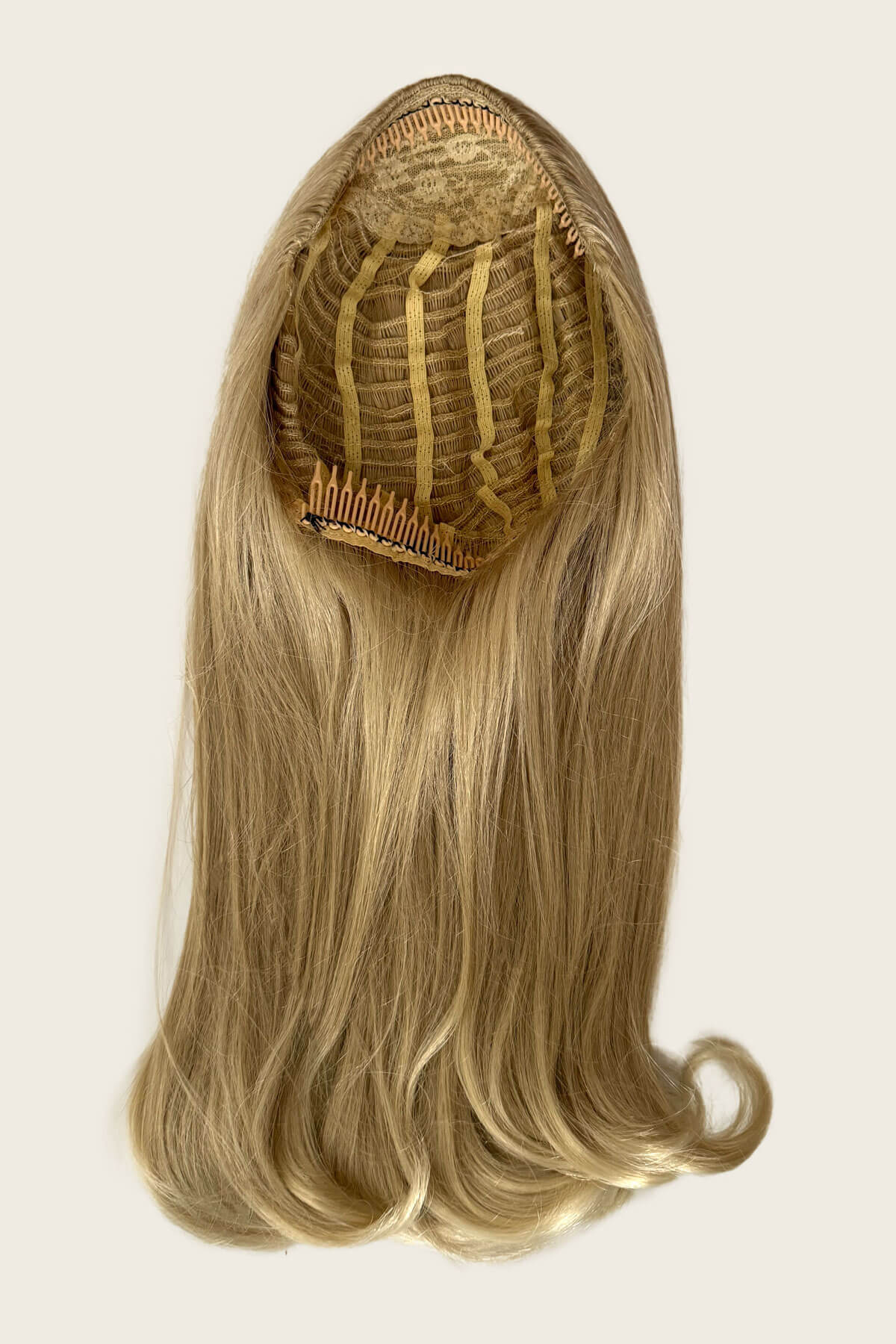 Blonde hair extension with a comb on a beige background. Blonde wig on a mannequin head against a plain background. 1960s Retro high crown, half wig hairpiece, long with hair flip: Priscilla blonde 613T24