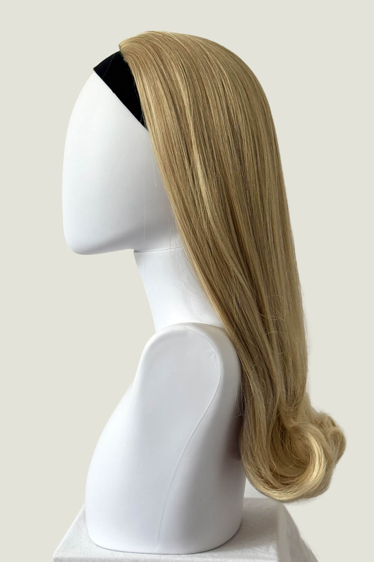 Blonde wig on a mannequin head against a plain background. 1960s Retro high crown, half wig hairpiece, long with hair flip: Priscilla blonde 613T24