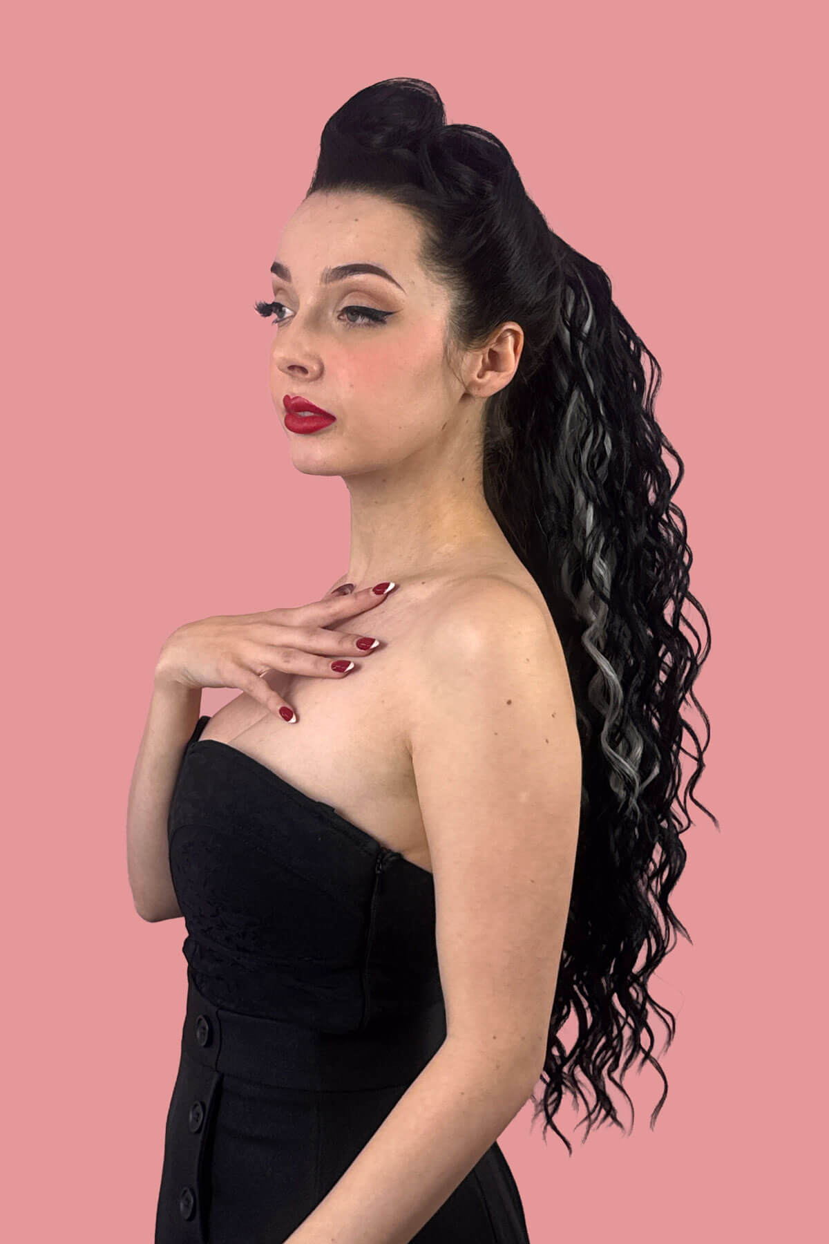 A woman in profile wearing a black strapless dress, showcasing a long, dark, curly wavy hair extension with grey streaks against a solid pink background. Long Curly Ponytail Hair Piece Extension, Black and Grey