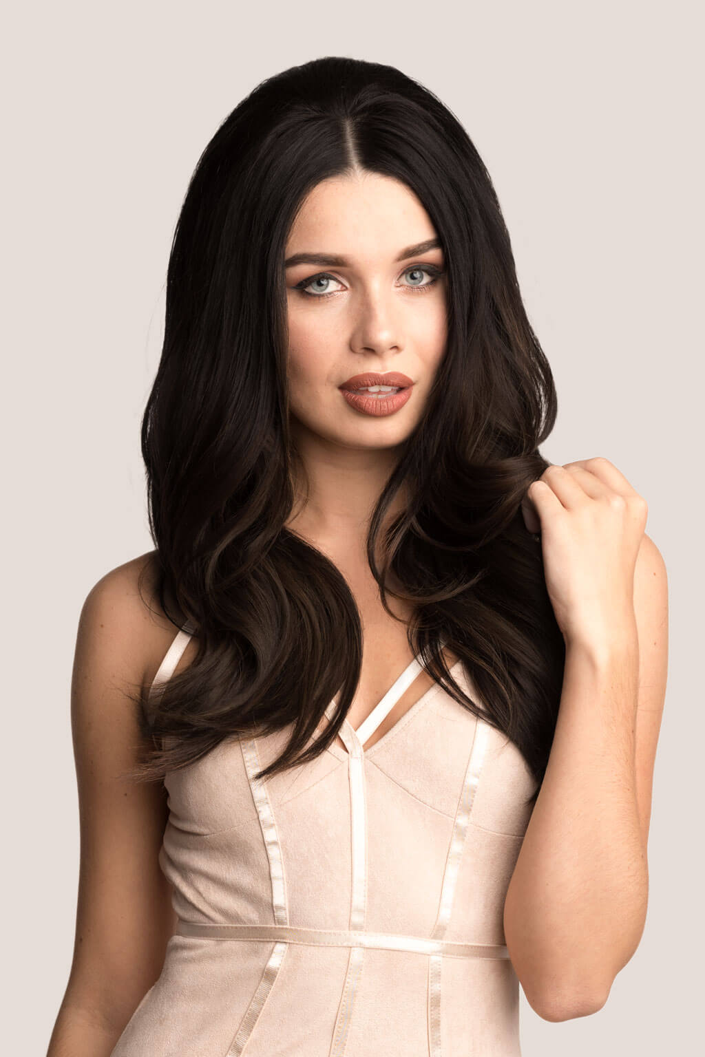 Woman with long, dark hair wearing a beige dress against a light background. Volume and Height Booster Hairpiece: Blaise