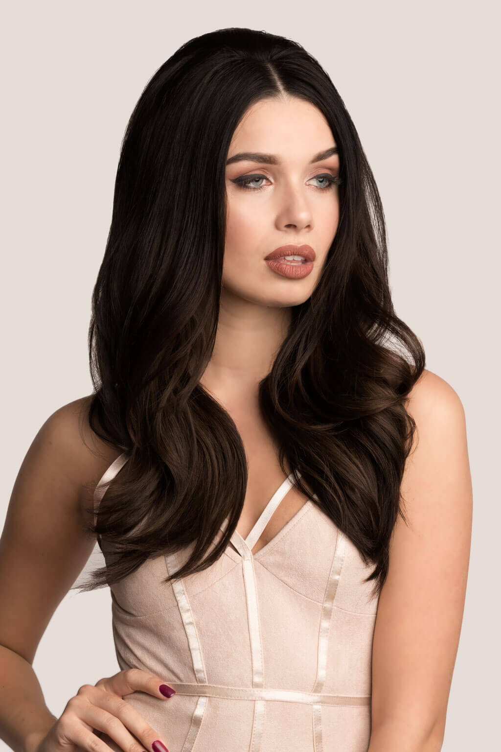 Woman with long, dark brown hair wearing a beige dress against a light gray background. Volume and Height Booster Hairpiece: Blaise
