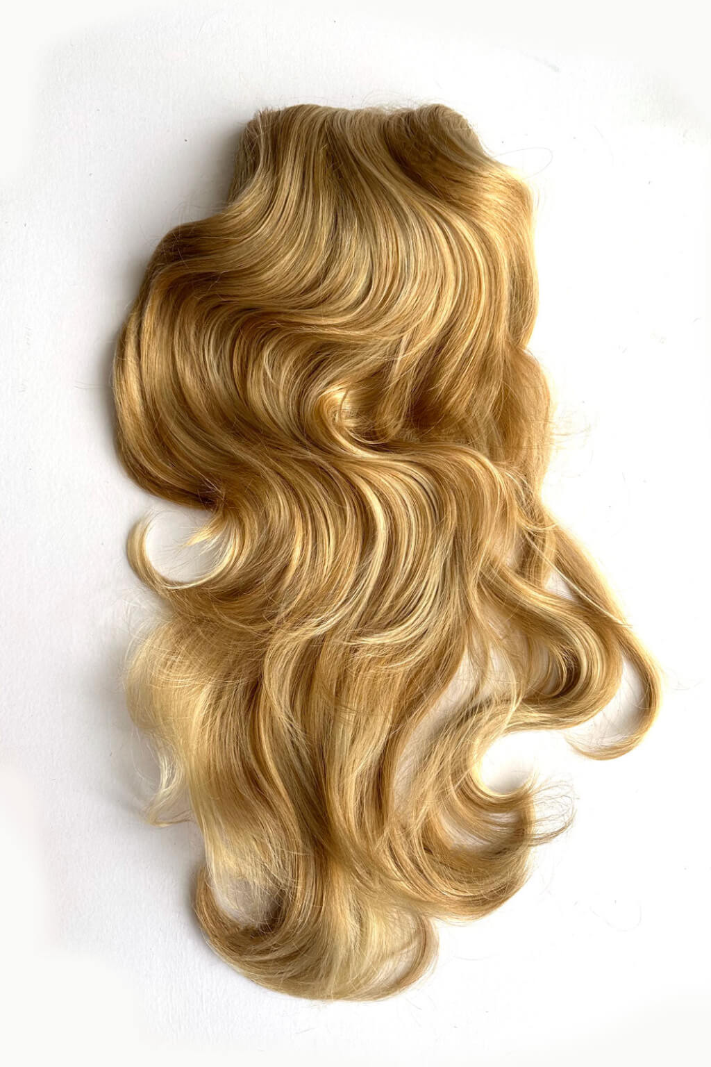 Long, wavy blonde hair extension or wig piece laid flat on a plain white background. Double volume hairpiece extension: Naomi warm blonde 24BH613
