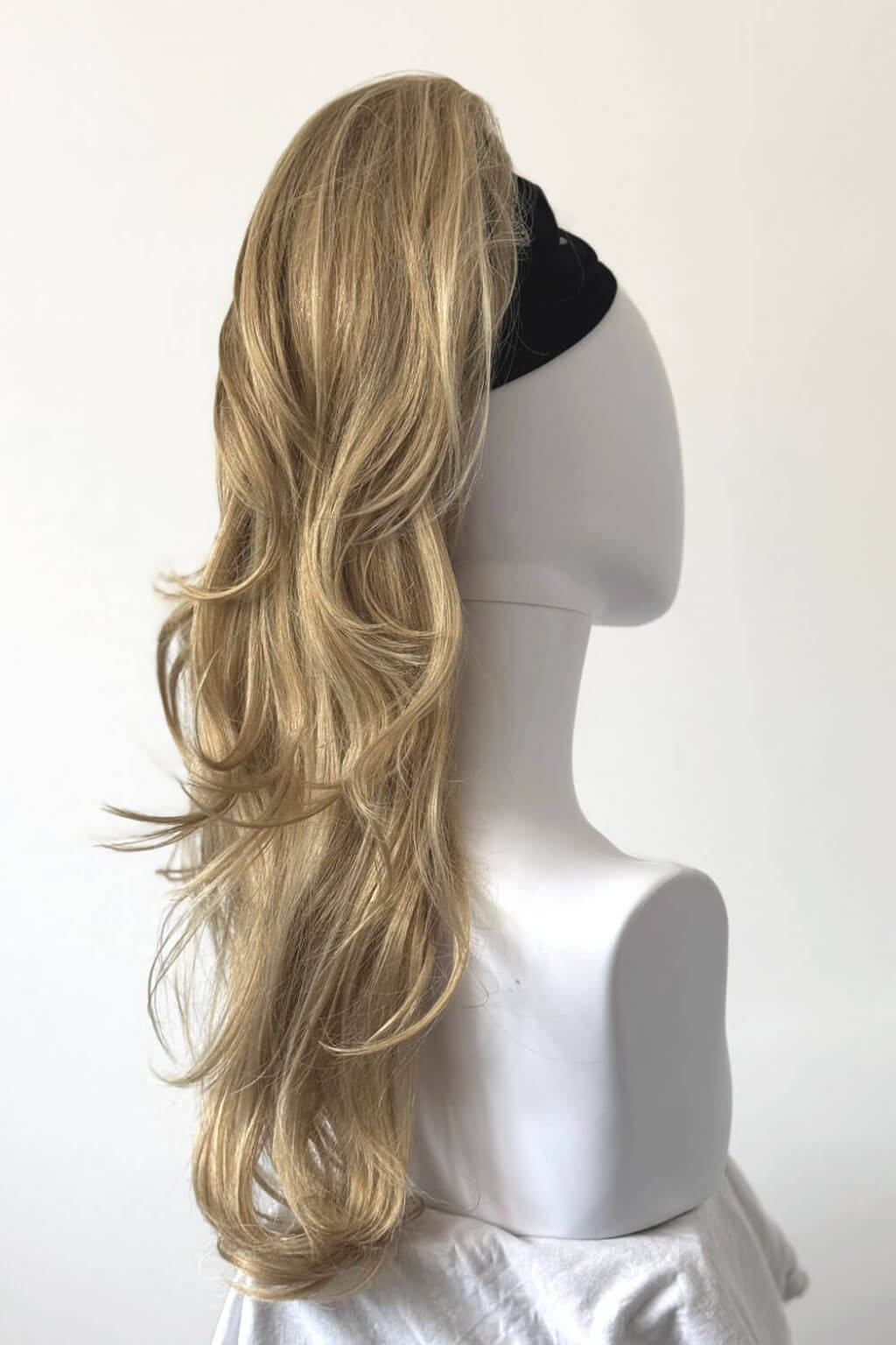 Blonde ponytail extension on a mannequin head against a white background. Clip-in ponytail hairpiece extension: Olivia blonde 24H613