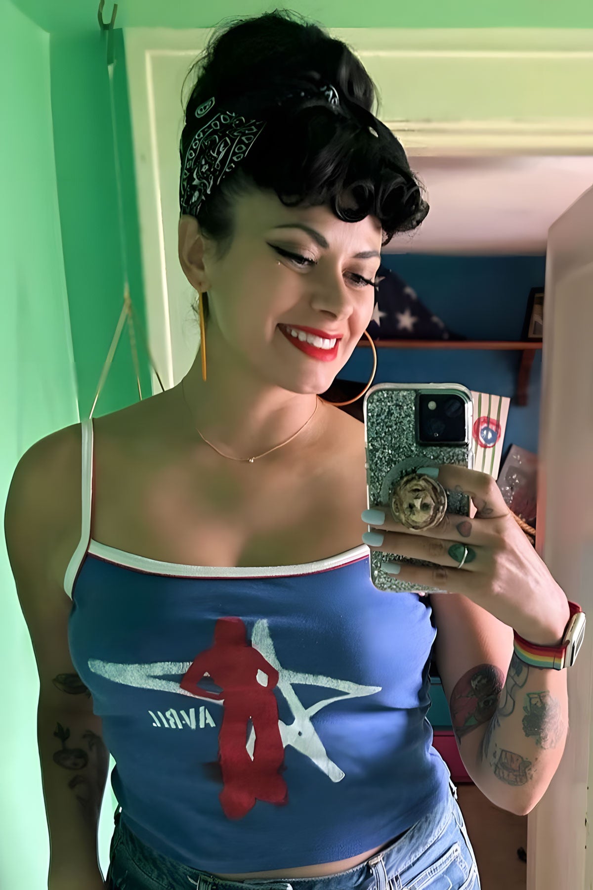 Woman taking a mirror selfie wearing a blue tank top with a red graphic design. Curly 1940s style clip-in fringe hairpiece/clip-in bangs: Bunny black 1B