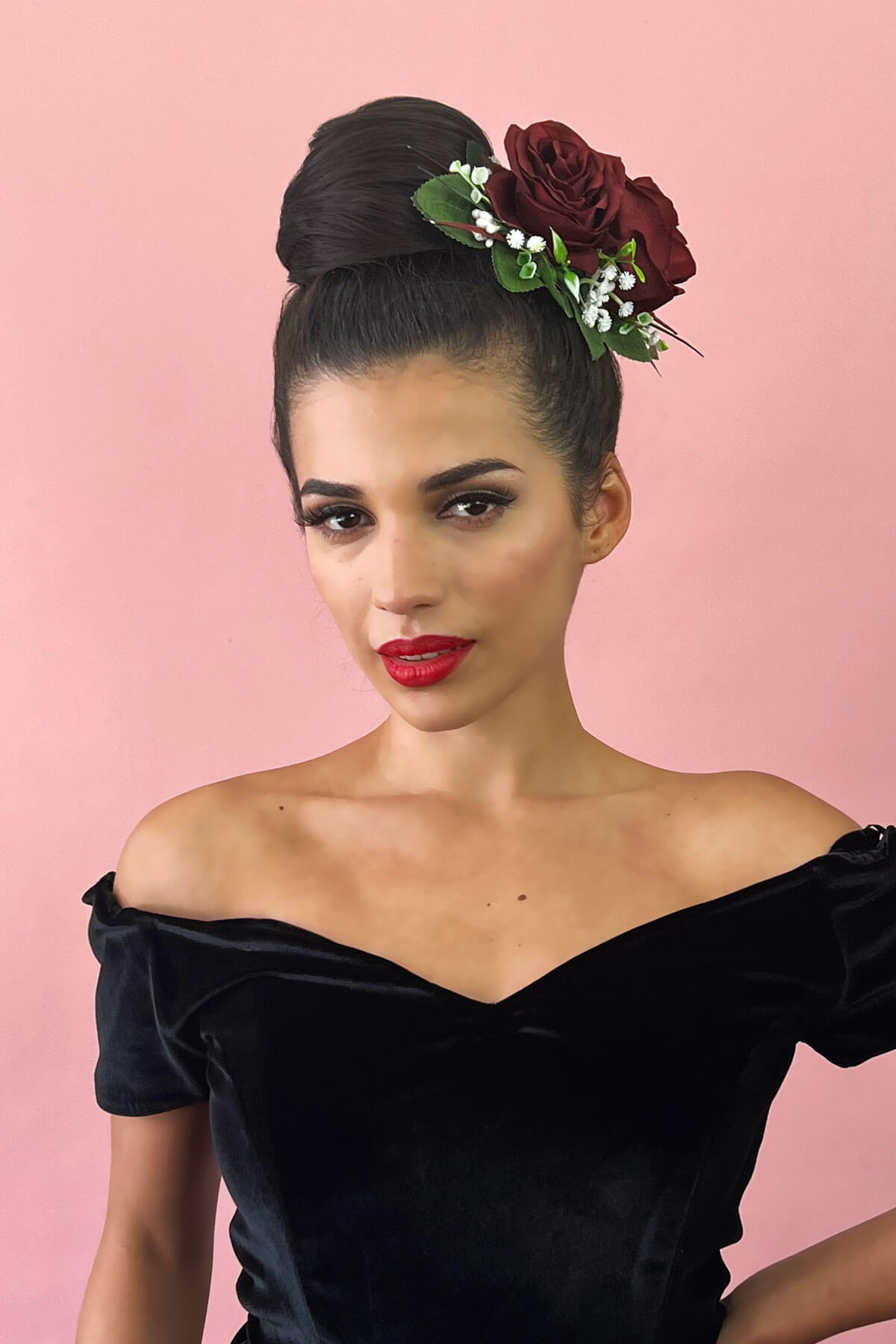Woman wearing a black velvet off-shoulder top with floral headpiece against a pink background